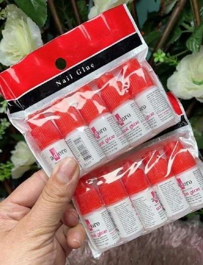 Mano sosteniendo dos paquetes de botellas de pegamento para uñas de color rojo y blanco