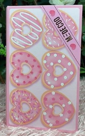 Donas rosas en forma de corazón con diferentes ingredientes en una caja con una cinta rosa etiquetada