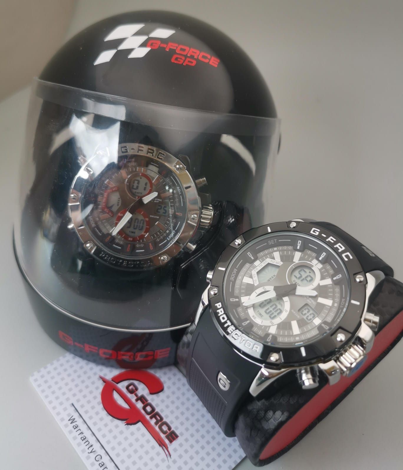 Dos relojes G-Force: uno dentro de una vitrina de casco negra y el otro sobre un soporte.