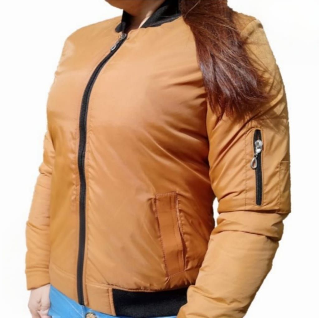 Mujer que lleva una chaqueta bomber color canela con ribete negro y cremallera cerrada.