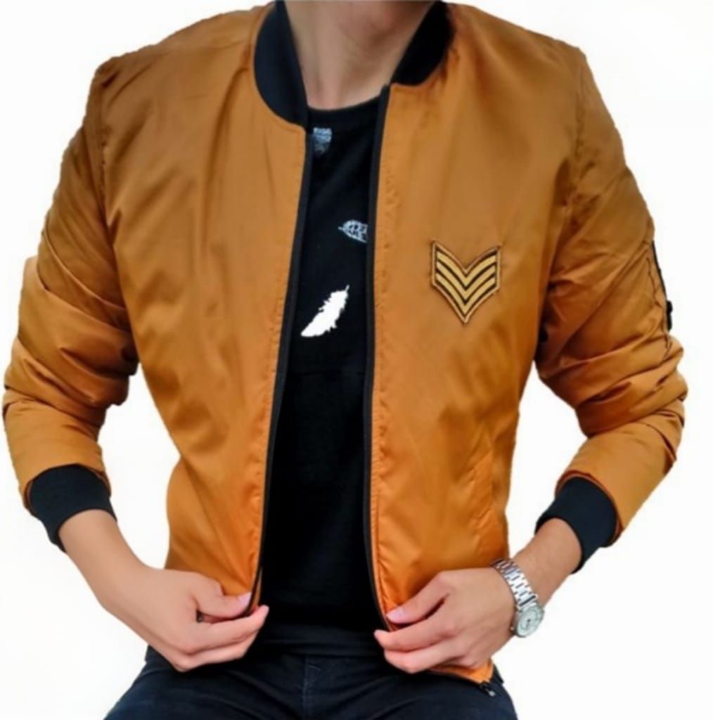 Hombre con chaqueta bomber gris claro sobre camisa negra, manos en los bolsillos, al aire libre.