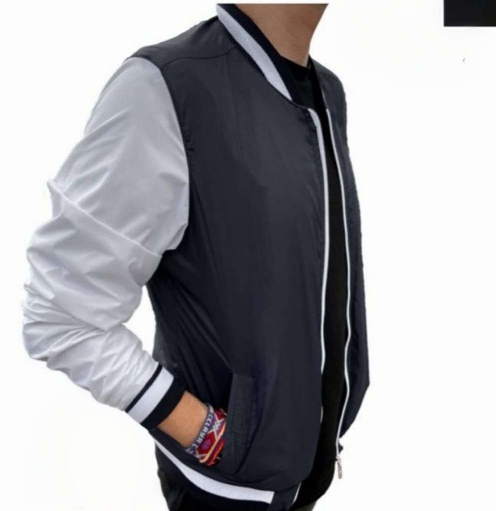 Hombre vestido con chaqueta bomber azul marino y blanca y camisa negra.