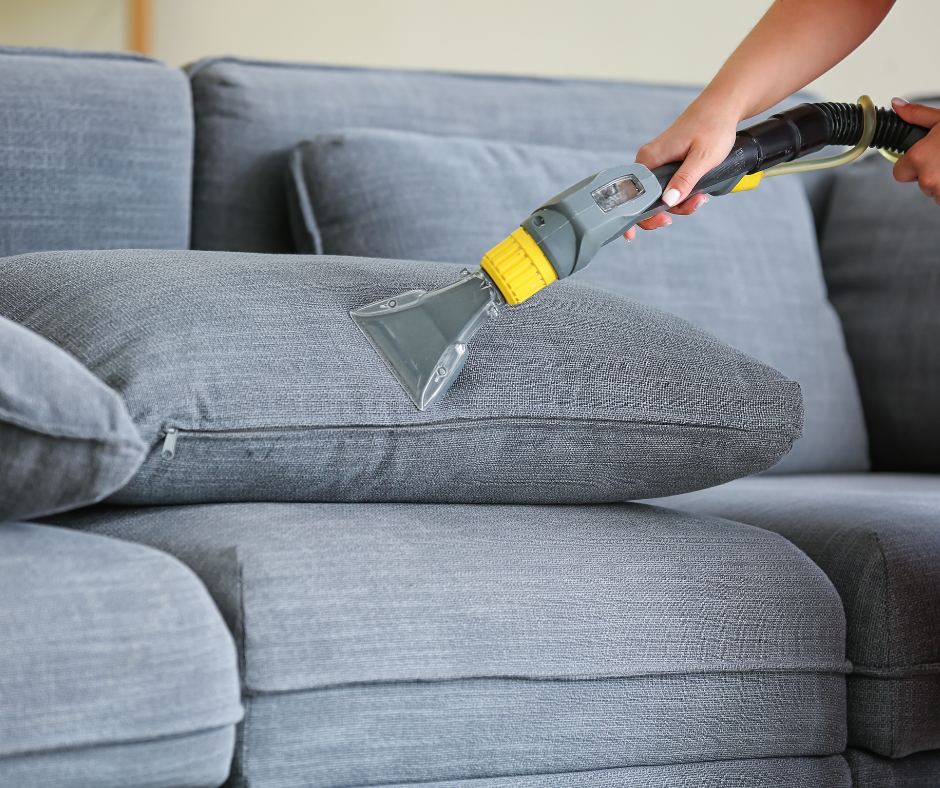 Une personne utilise un nettoyeur de tissus d'ameublement portatif sur un coussin de canapé gris, à l'intérieur.