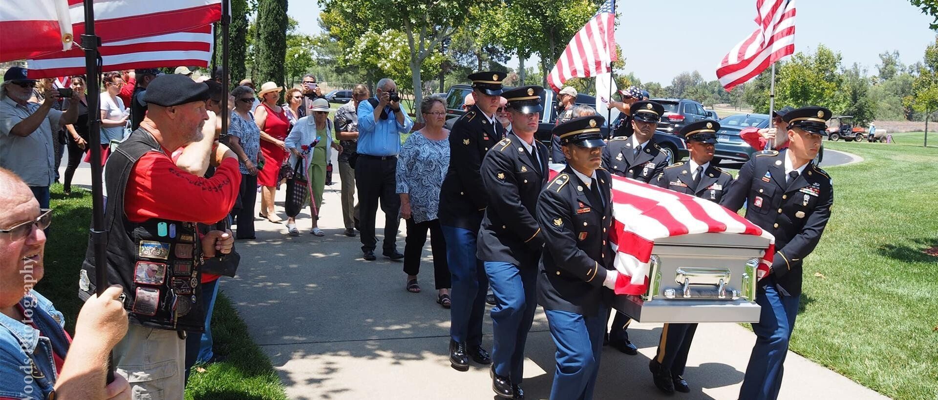 Uniformed honor guard carrying a U.S. flag-draped casket in a cemetery procession