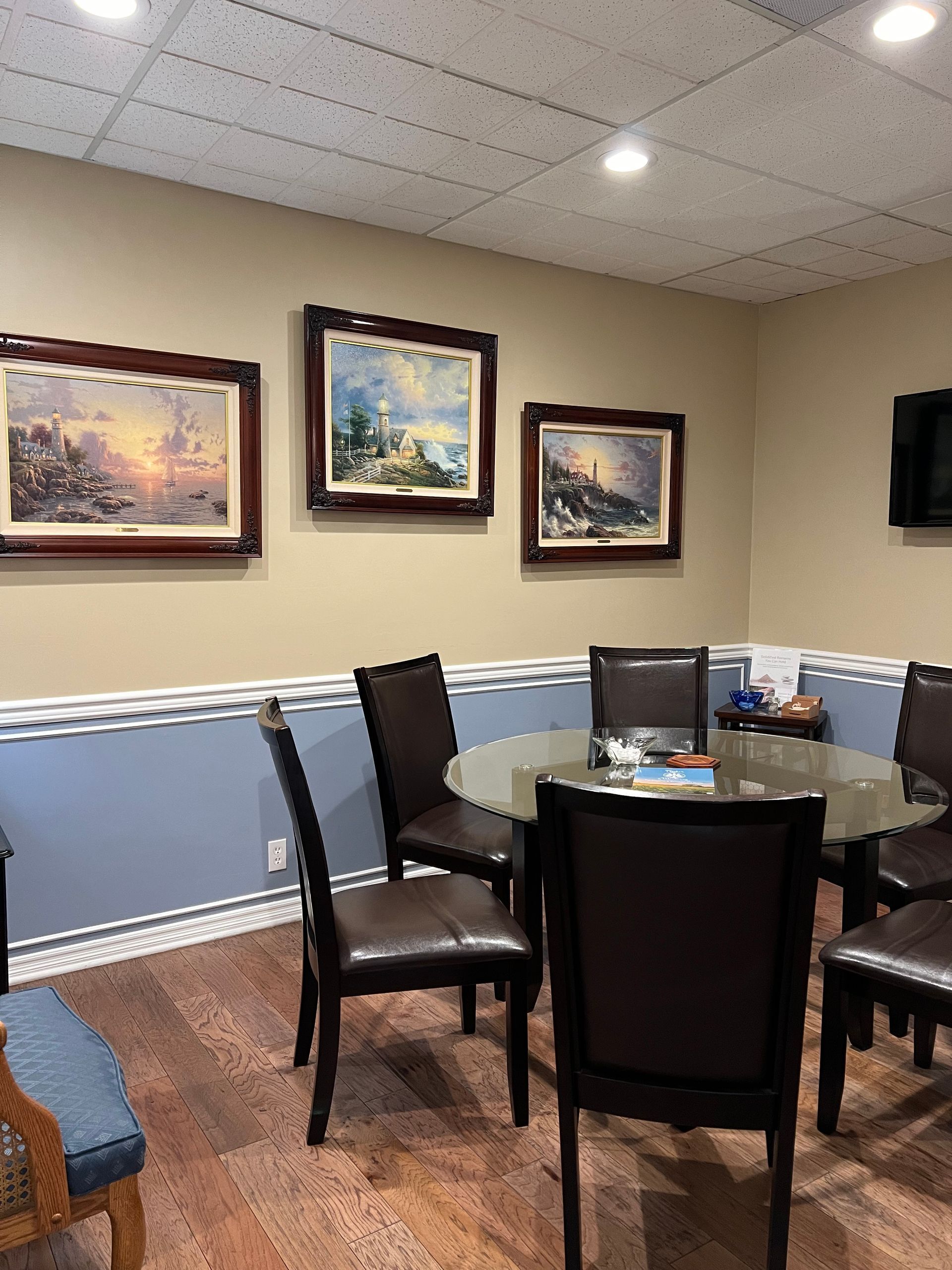 Restaurant seating area with round table, dark chairs, framed wall art, and blue wainscoting