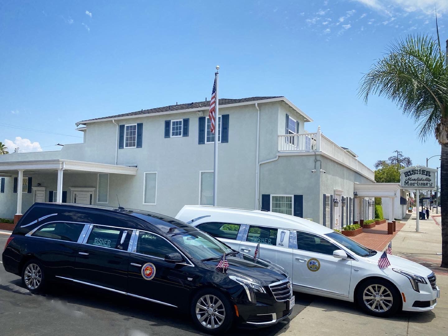 Two parked cars in front of a white building with an American flag under a blue sky