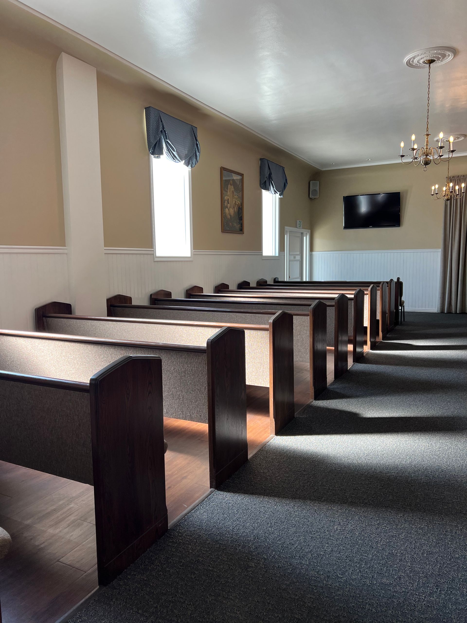 Empty church sanctuary with wooden pews, carpeted aisle, and a wall-mounted TV at the front