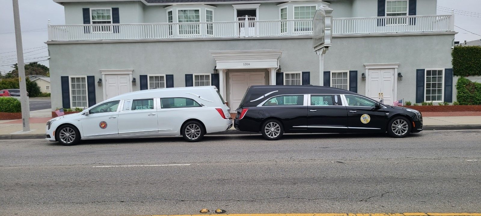 Two parked station wagons, white and black, in front of a gray building