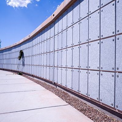 Curved concrete wall with metal panels and a small hanging plant along a paved walkway