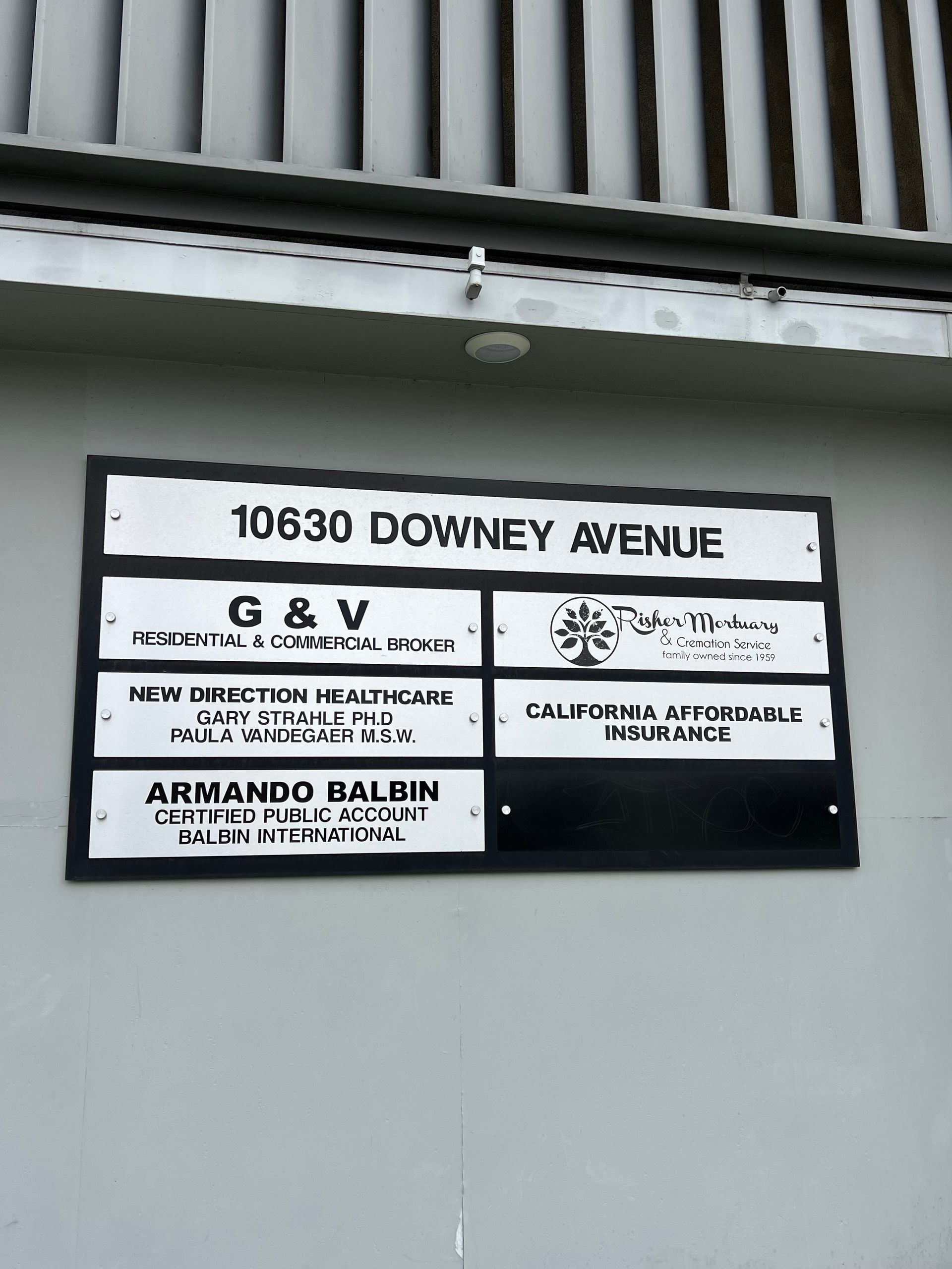 Office sign on a gray wall at 10630 Downey Avenue, listing G&V and service details.