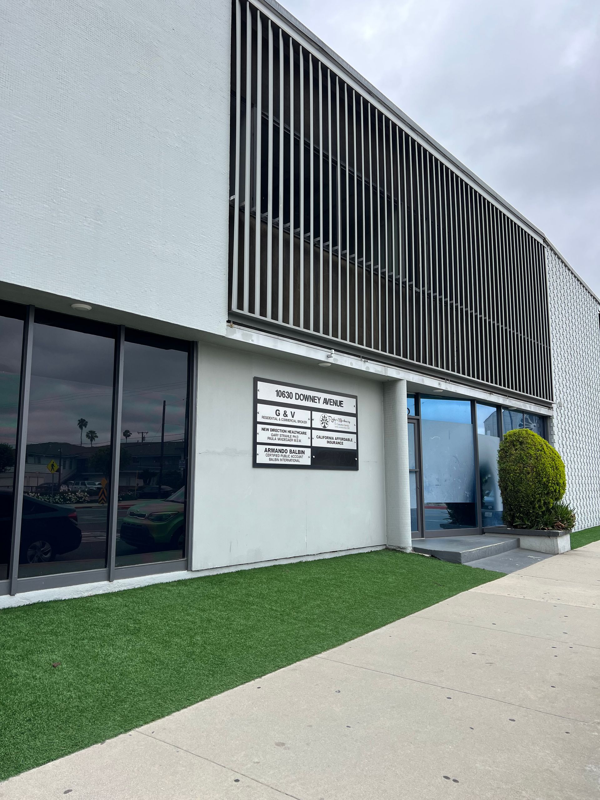Modern building exterior with black slatted facade, windows, and a sidewalk beside artificial grass.