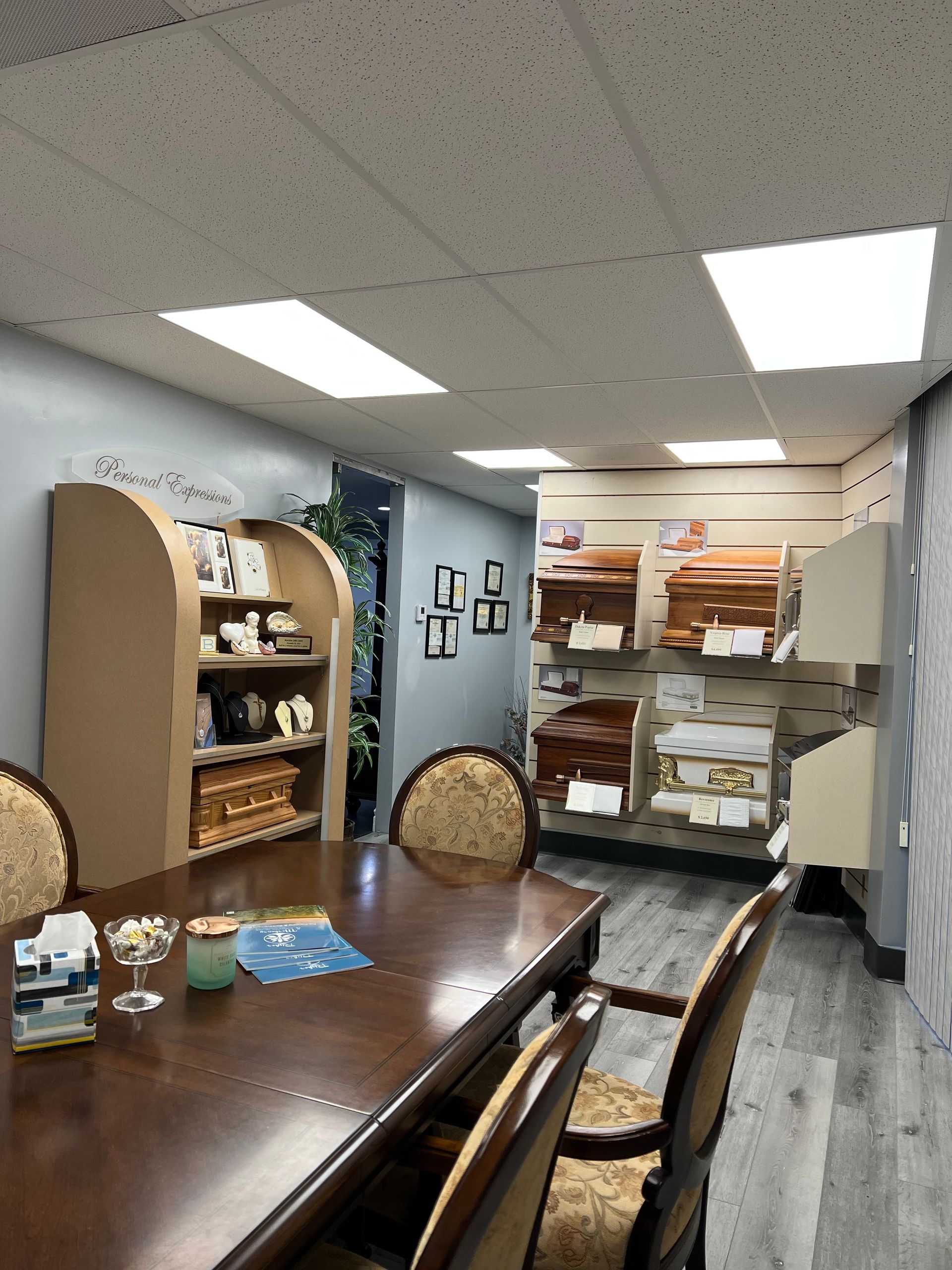 Small office meeting room with a wooden table, chairs, shelves, and ceiling lights.