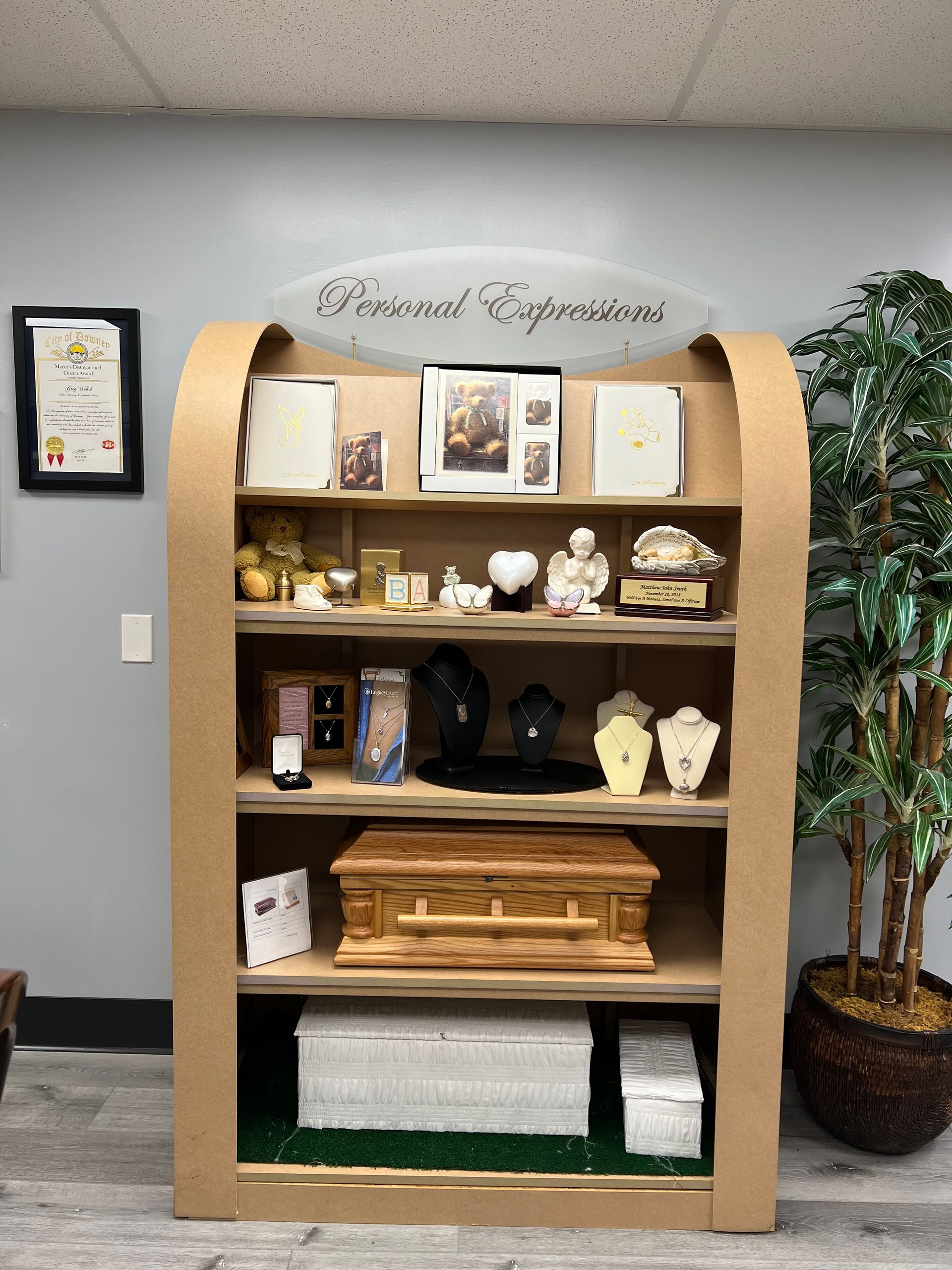 Wooden memorial display shelf with candles, framed photos, flowers, and a central urn in a quiet room