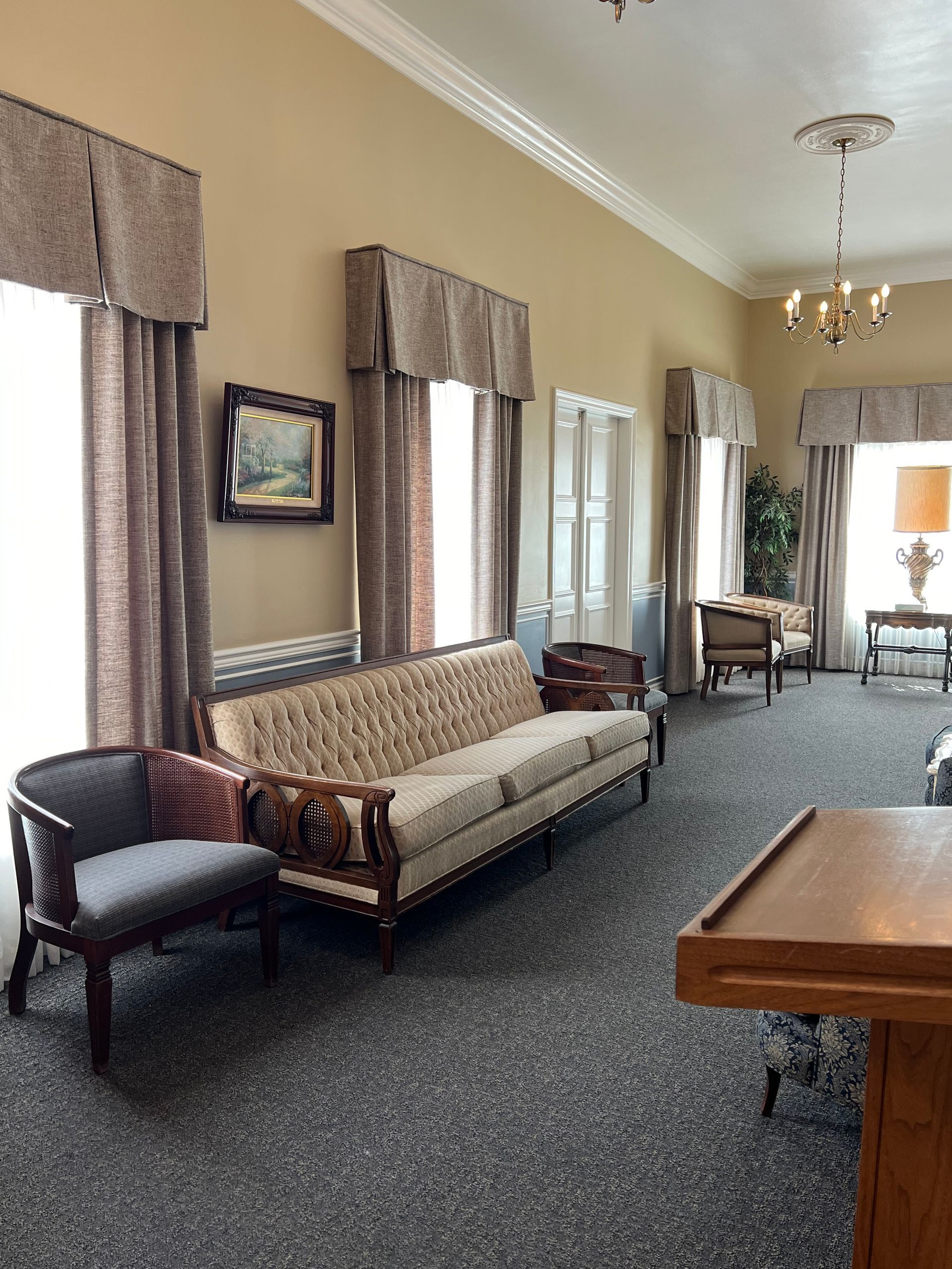 Quiet waiting room with patterned sofa, chairs, chandeliers, and carpeted hallway in beige tones