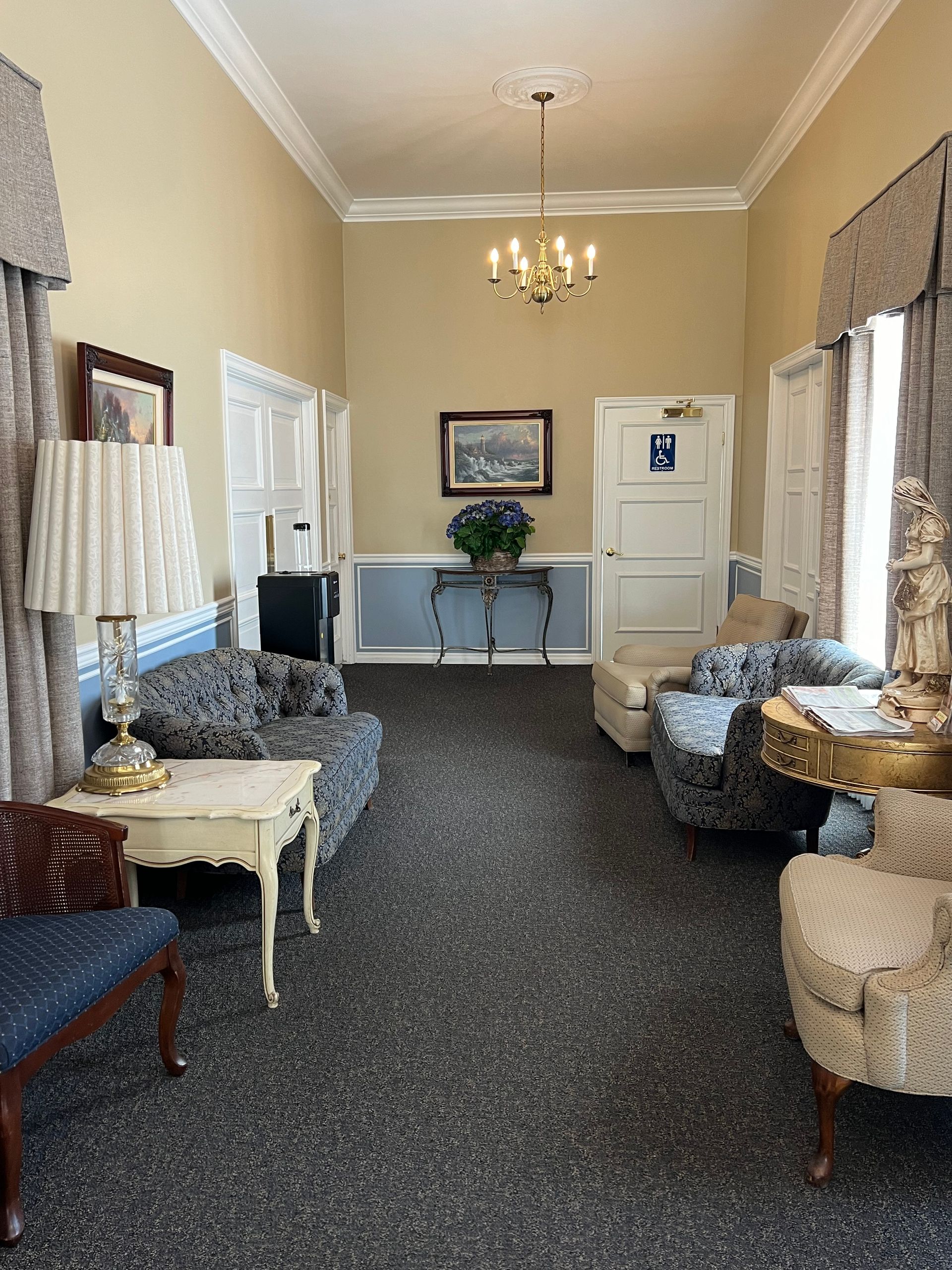 Elegant beige sitting room with patterned chairs, chandelier, and windows with curtains.