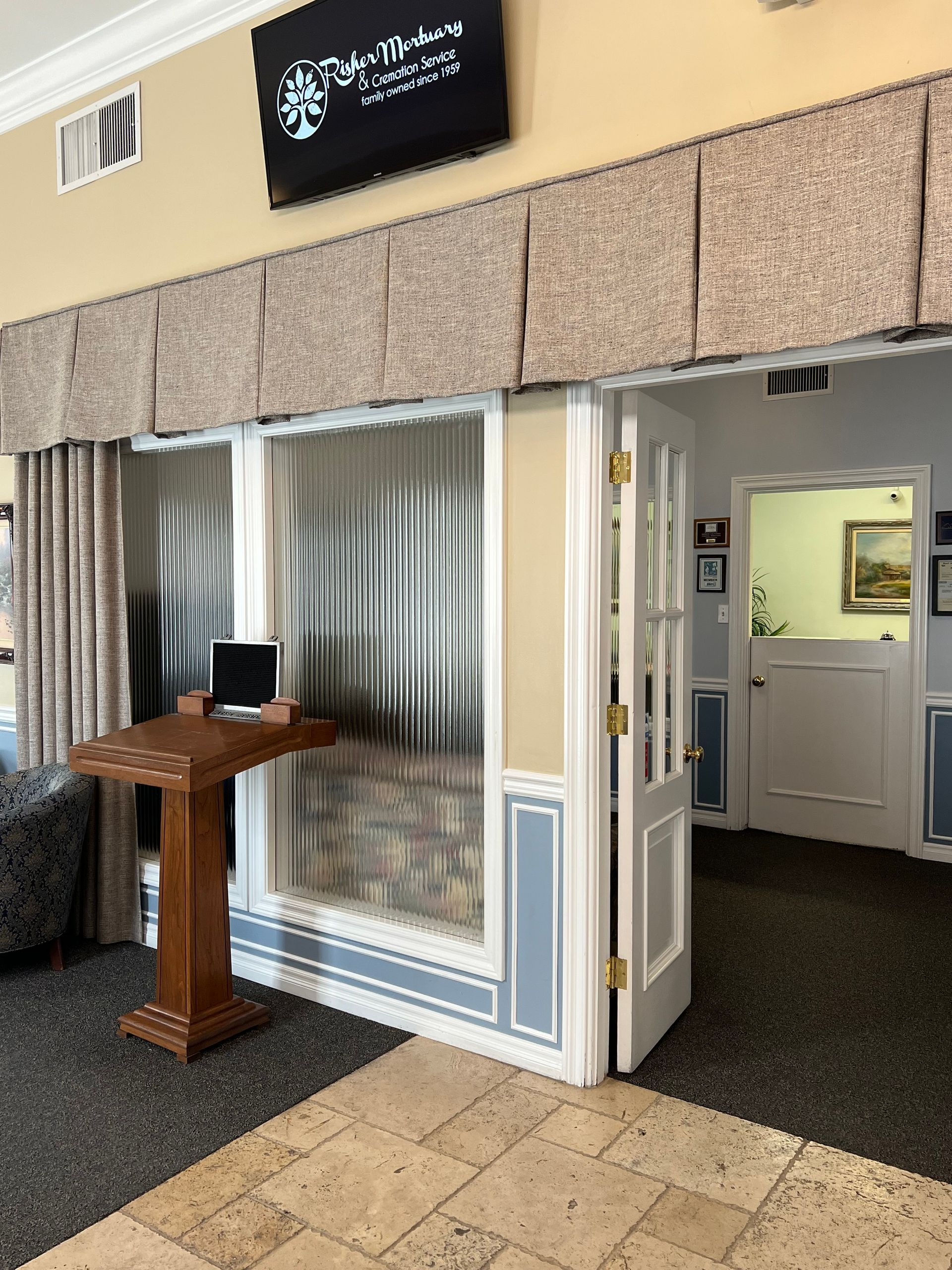 Lobby entrance with open white doors, a wooden podium, and a small sign above a striped wall.
