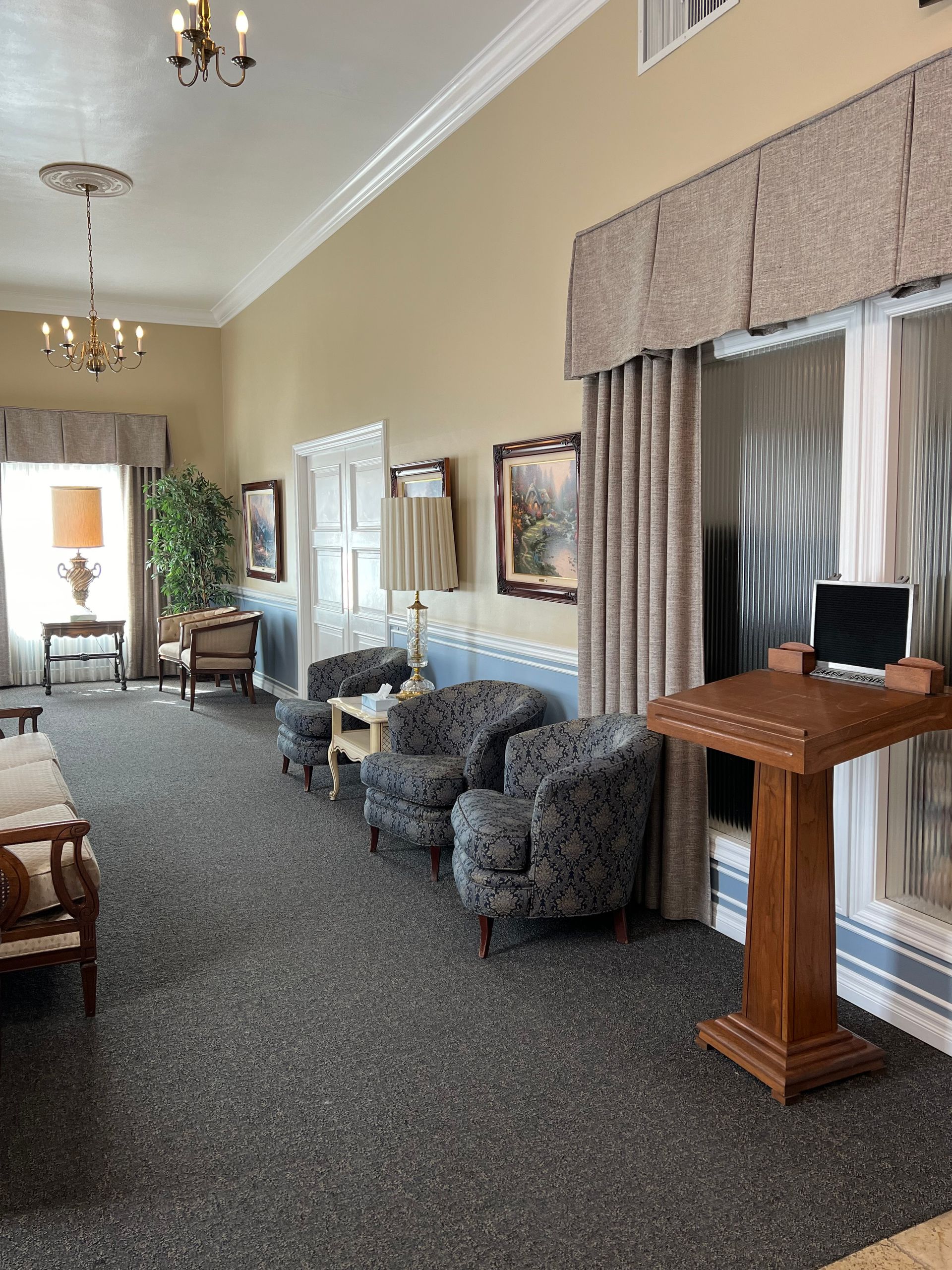 Elegant lounge with gray chairs, wooden podium, chandelier lighting, and tall windows with drapes