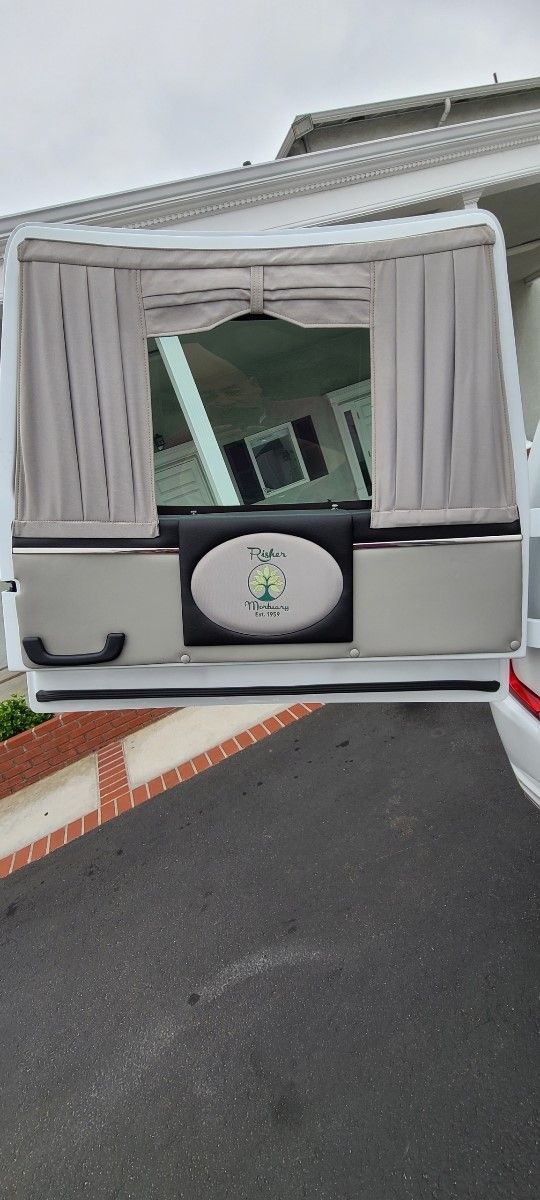 Fold-out camper trailer rear with curtains, table, and a bicycle wheel visible inside, parked on a driveway.