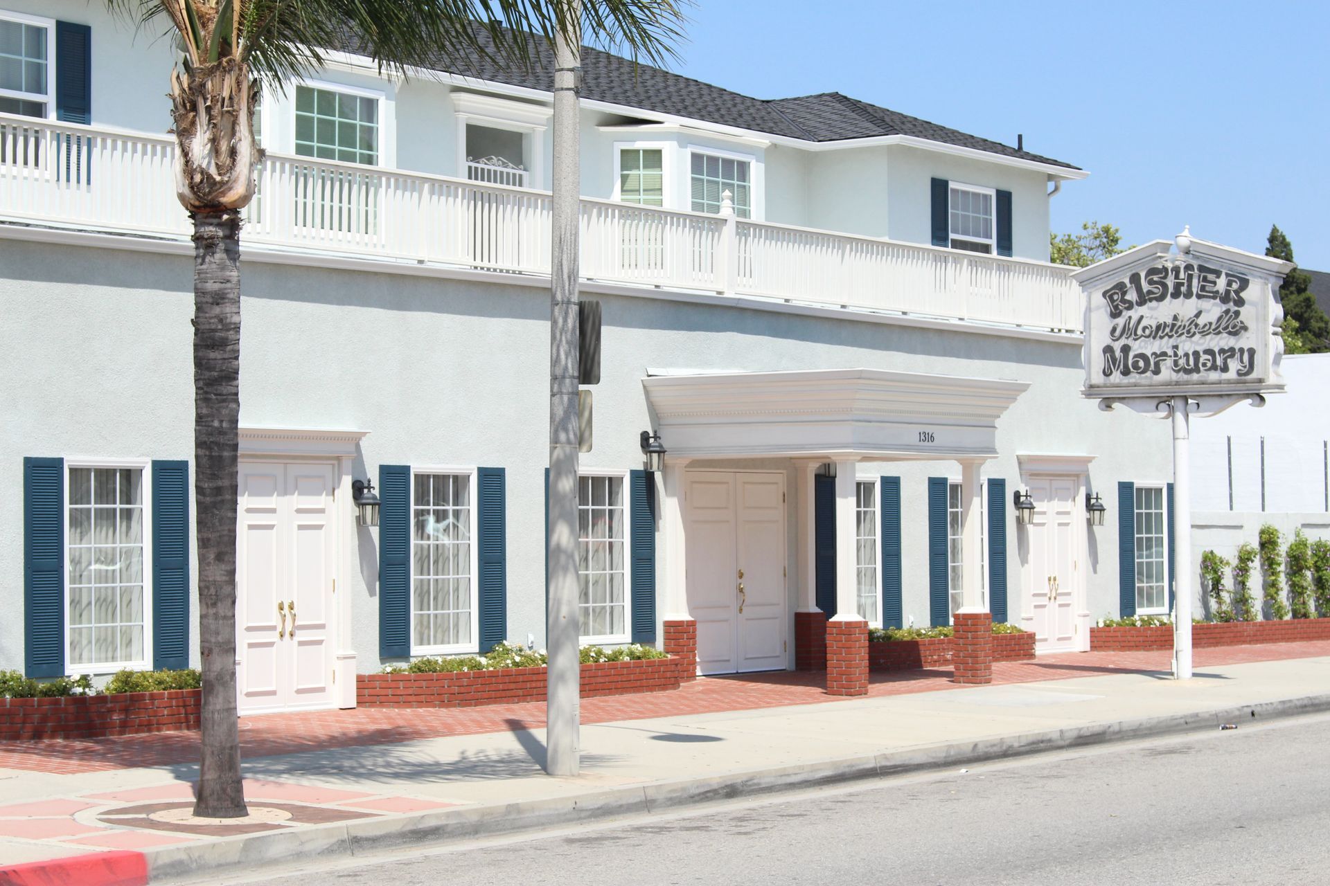 White two-story building with blue shutters and a sign reading “The Marigny” on a sunny street