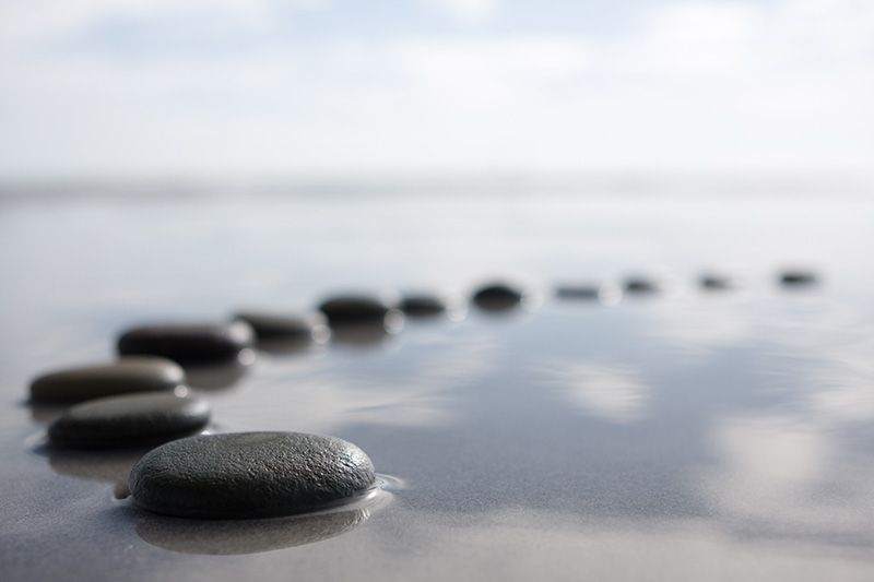 Black stones in a line on wet sand by calm water under a cloudy sky