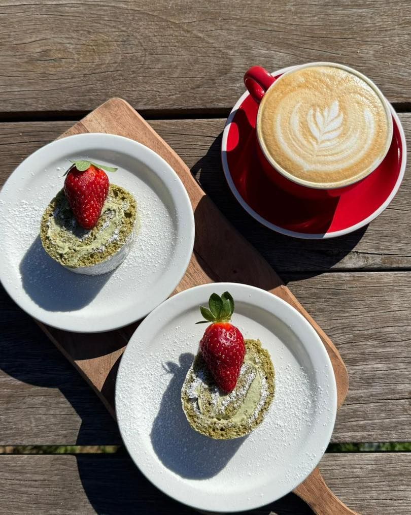 Two matcha cakes with strawberries, coffee art latte in a red cup on a wooden board.