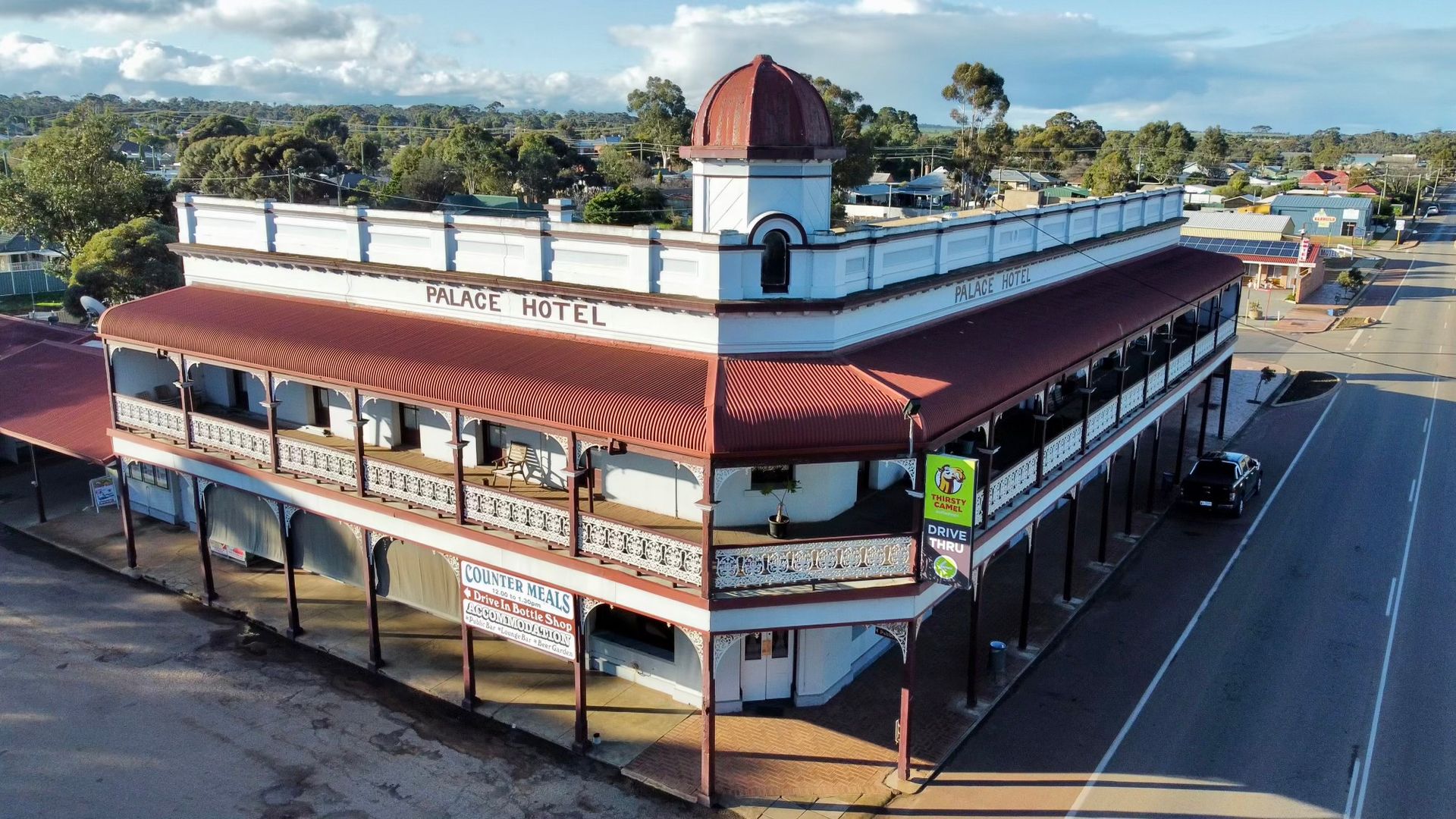 Two-story white hotel with a red roof and a corner turret, located on a street, small town setting.