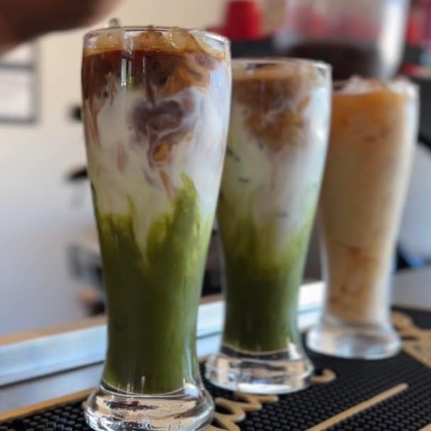 Three layered iced drinks in tall glasses. Green matcha, white milk, and brown coffee.