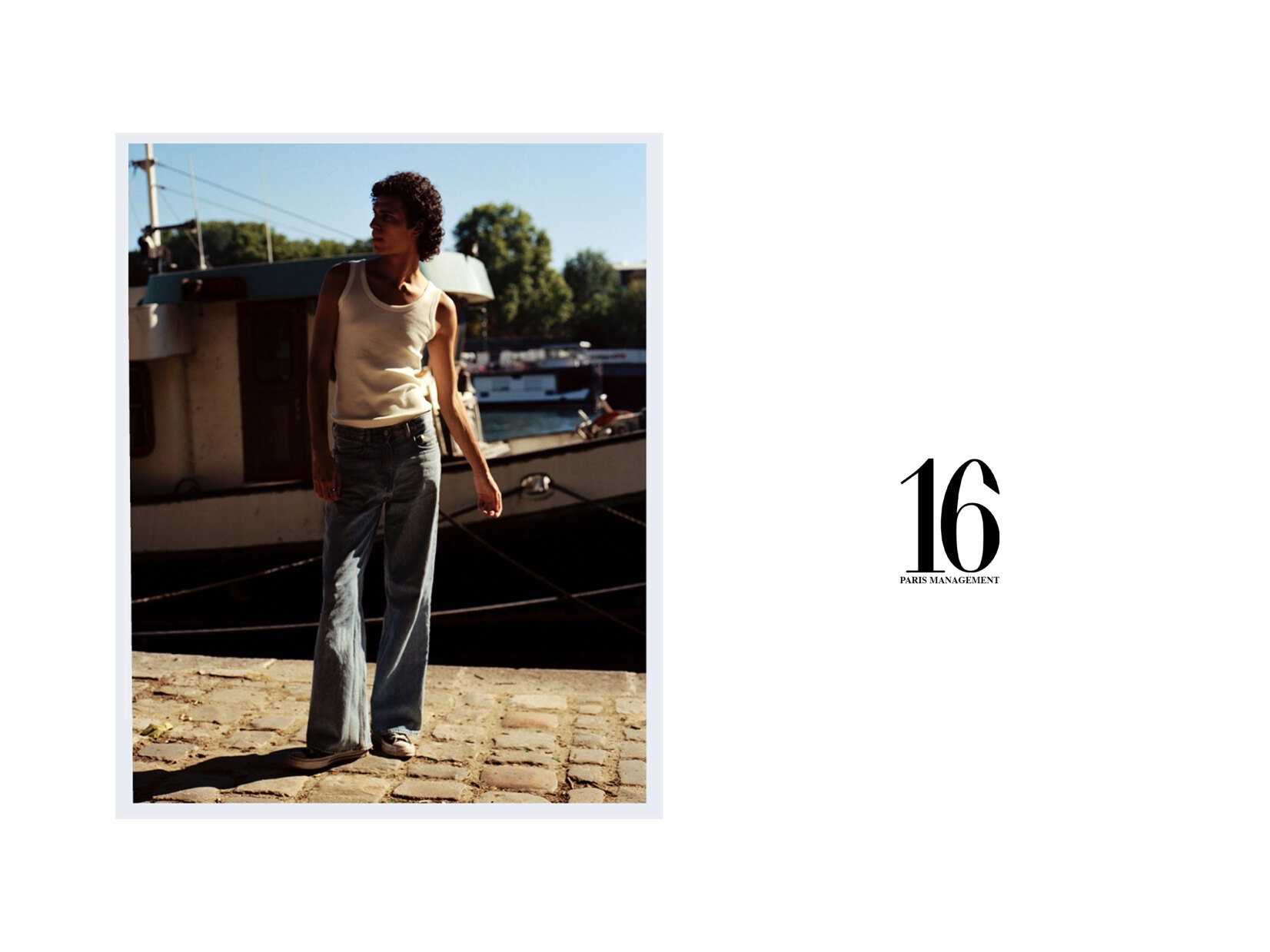 Mann in weißem Tanktop und Jeans steht an einem sonnigen Tag neben einem Boot.