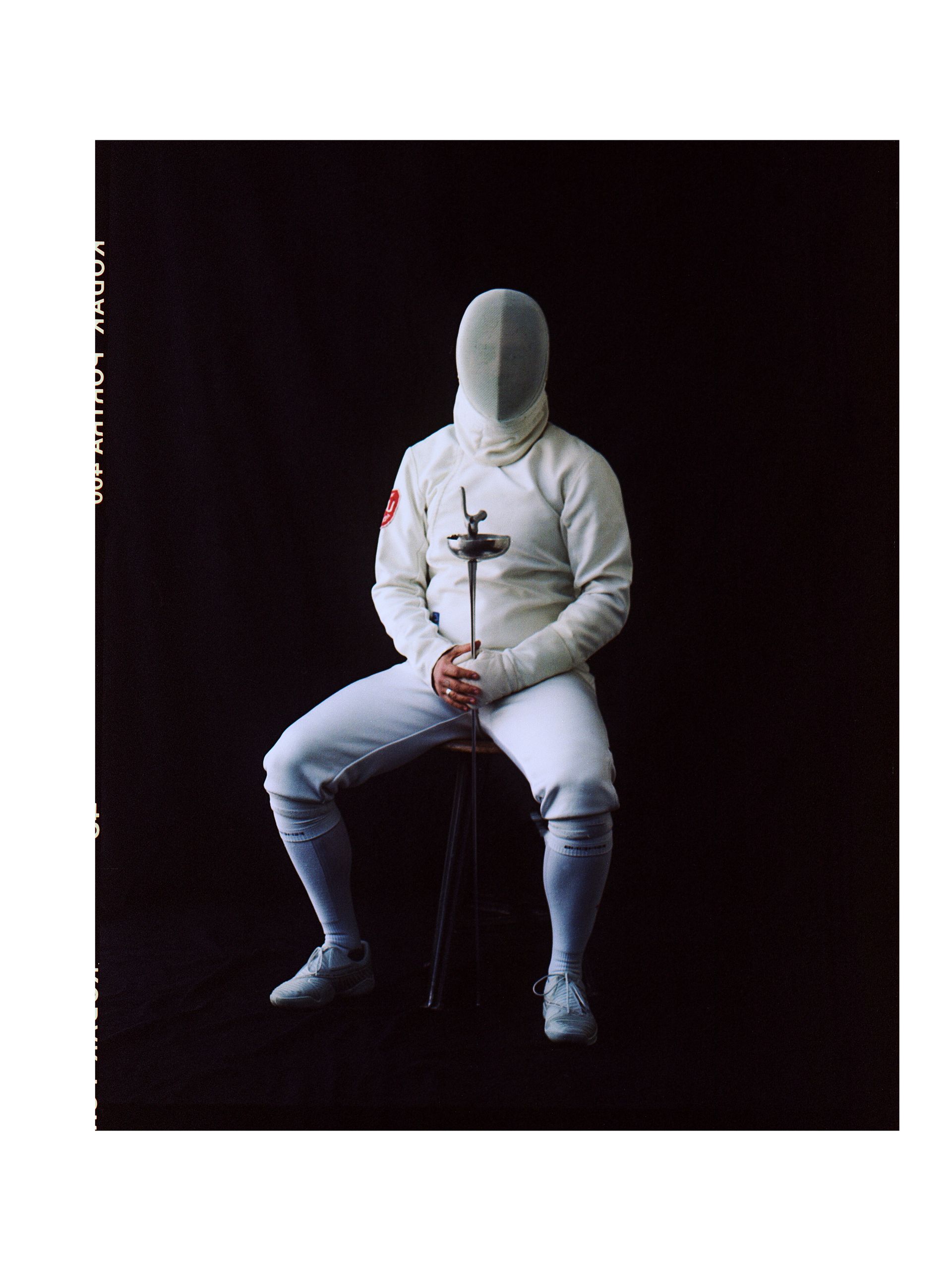 Fechter in weißer Uniform, Florett haltend, auf einem Hocker vor schwarzem Hintergrund sitzend.