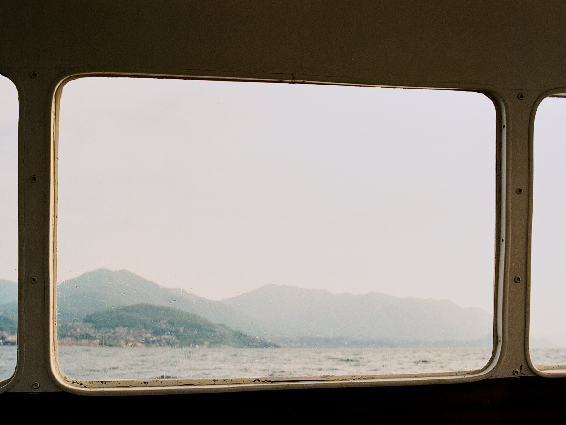 Blick auf die Berge auf der anderen Seite des Meeres durch ein Bootsfenster an einem dunstigen Tag.