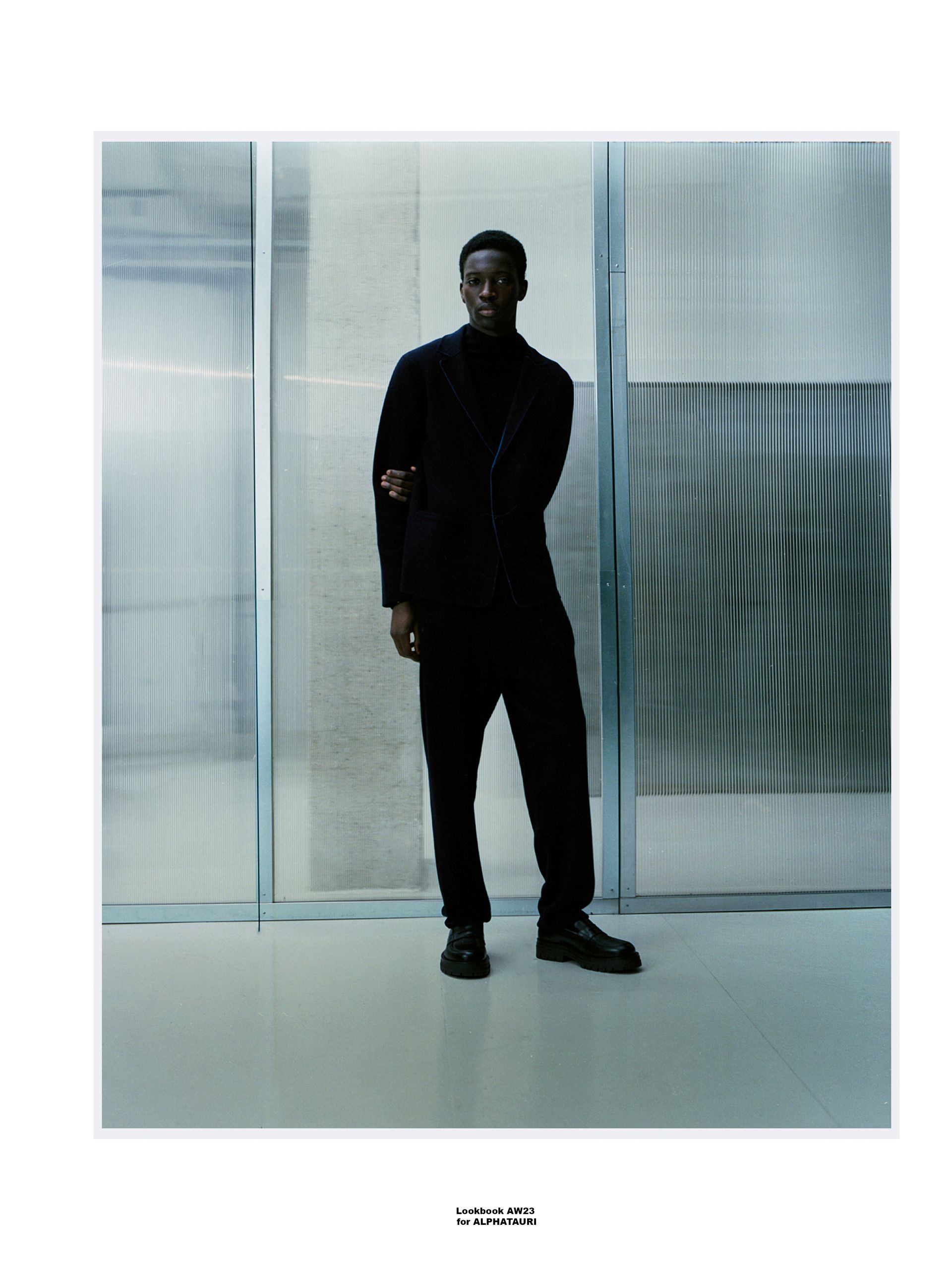 Ein Mann im schwarzen Anzug steht vor einer Wand mit silberner, gewellter Textur.