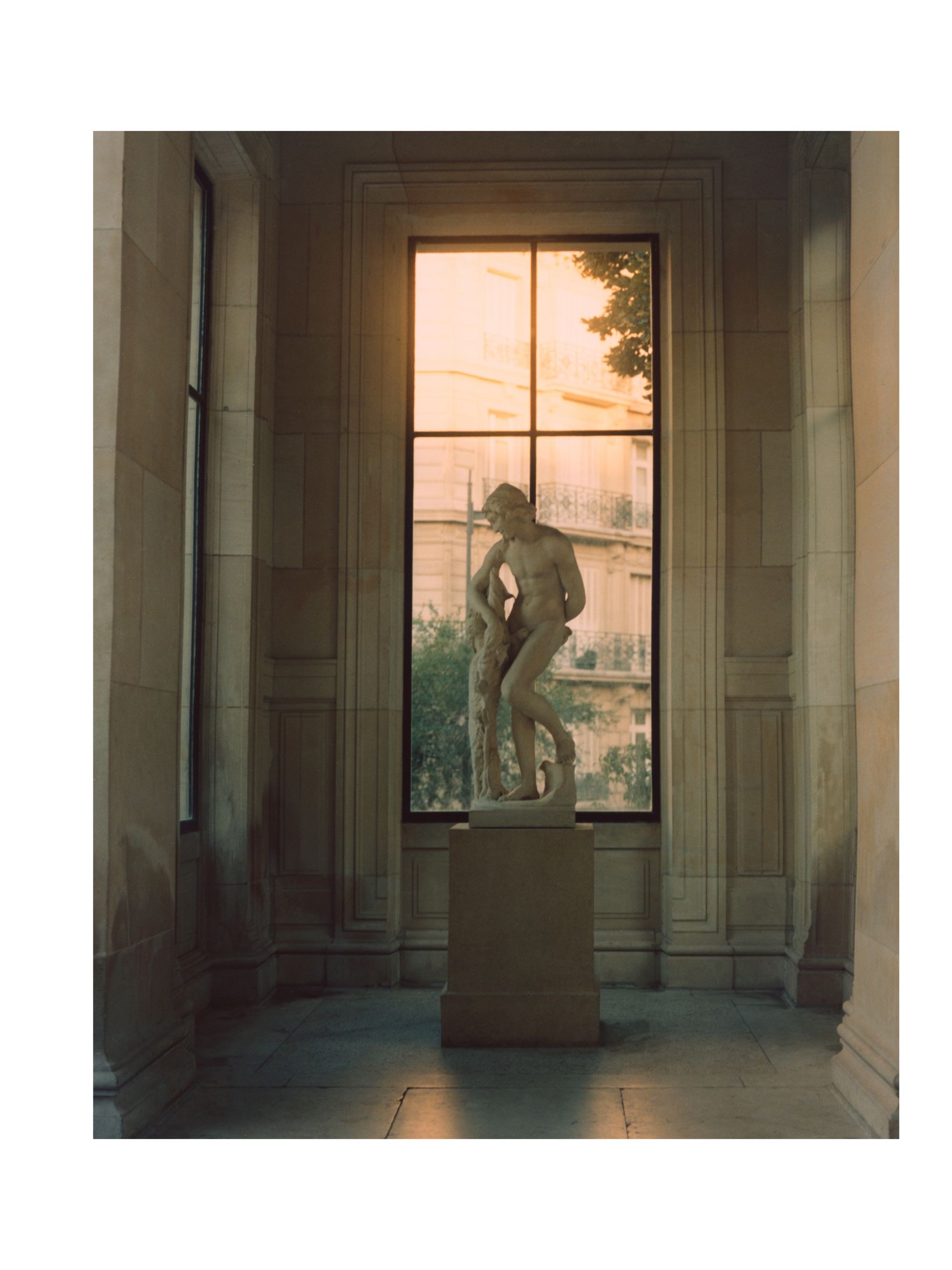 Statue im Fenster; Licht strömt auf die Skulptur und den Steinraum.
