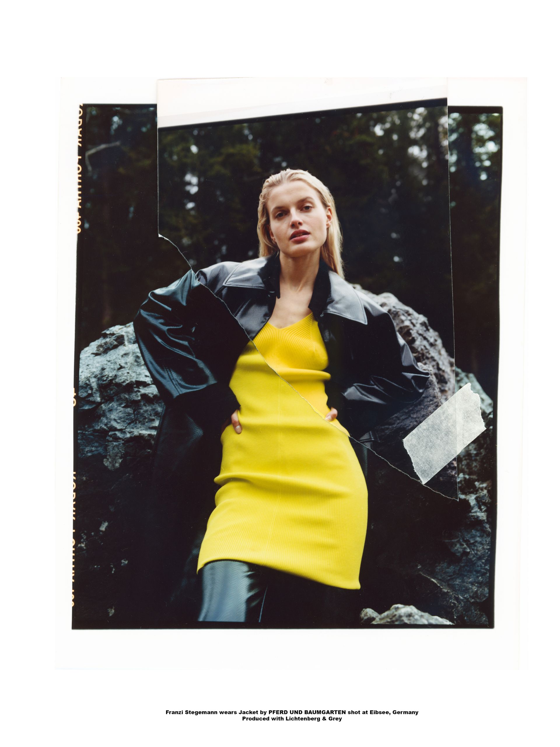 Frau in gelbem Kleid und schwarzem Mantel steht vor Felsen in einem dunklen Wald.