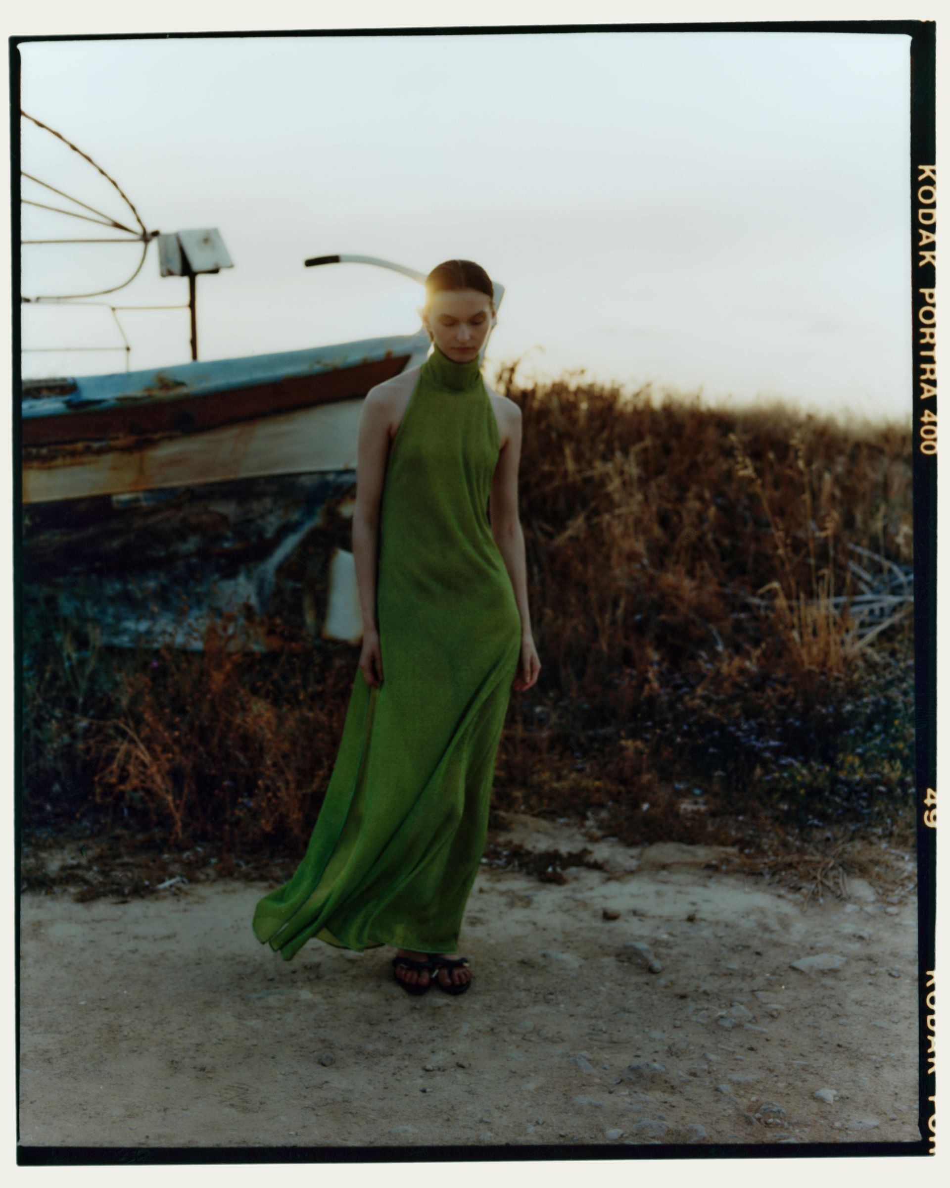 Frau im grünen Kleid steht bei Sonnenuntergang auf einem Feldweg in der Nähe eines Bootes.