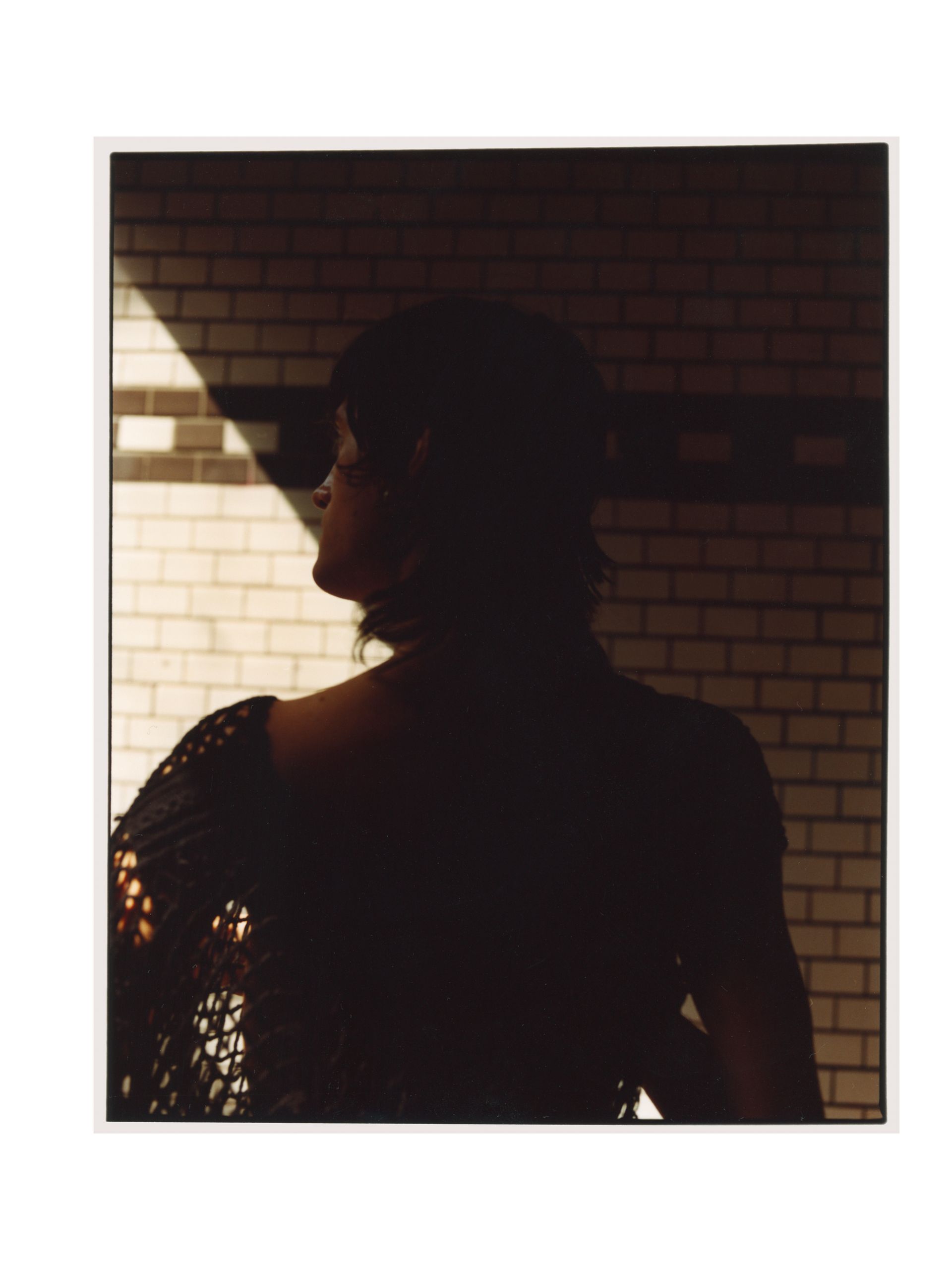 Silhouette einer Person, teilweise vom Sonnenlicht beleuchtet, vor einer Ziegelwand.