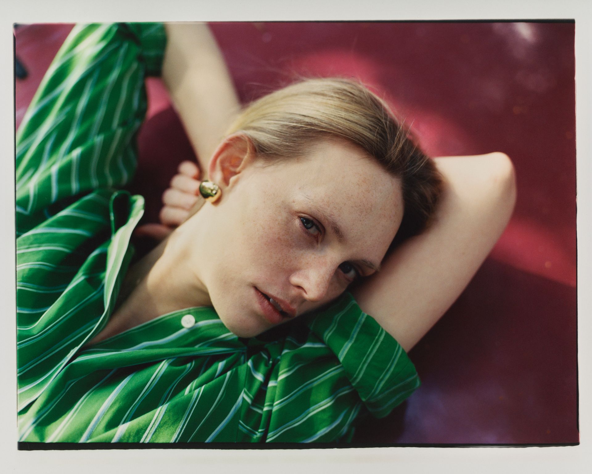 Frau in grün gestreiftem Hemd, ruht auf einer roten Fläche und blickt den Betrachter an.