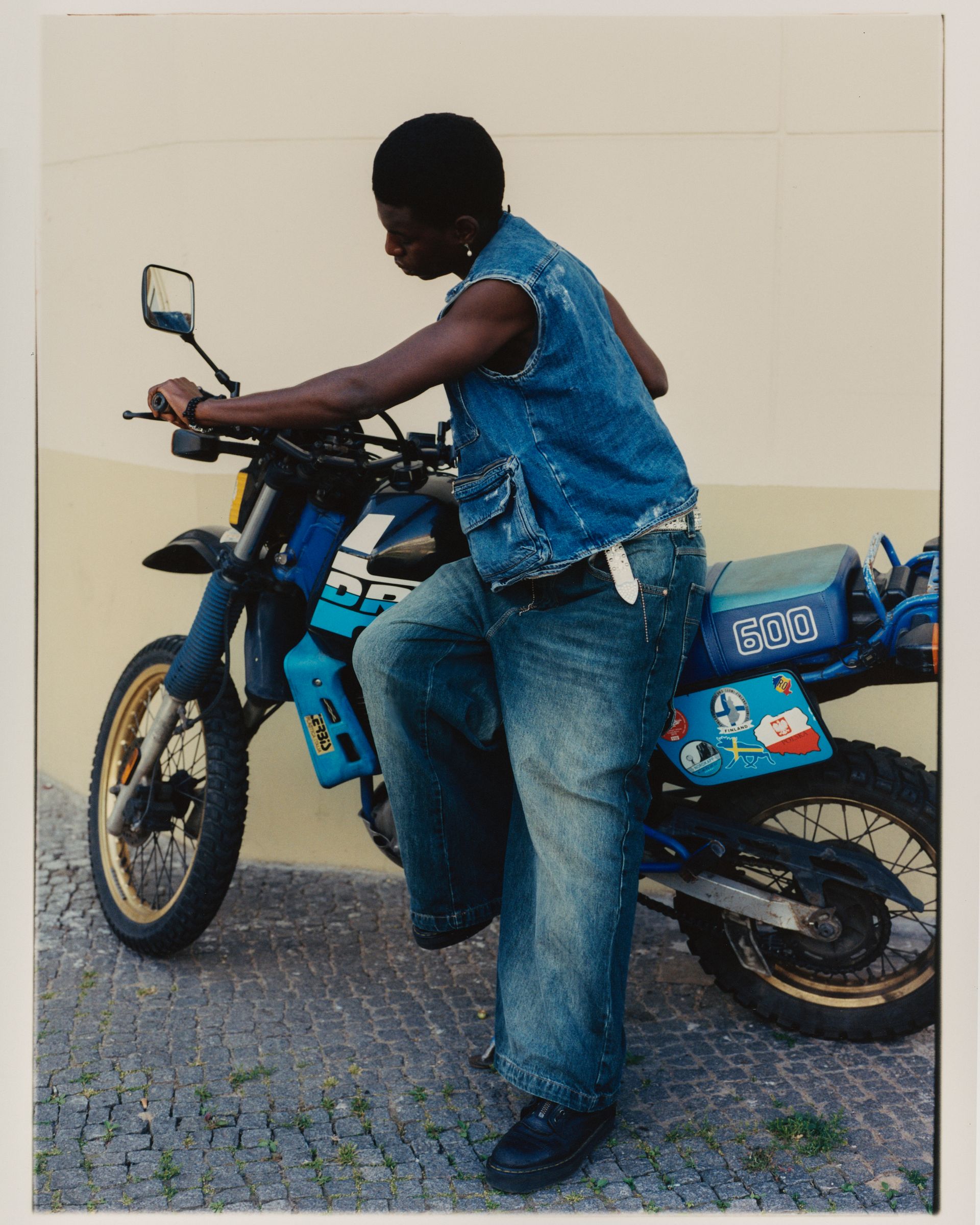 Person im Jeans-Outfit steht neben einem blauen Motorrad.