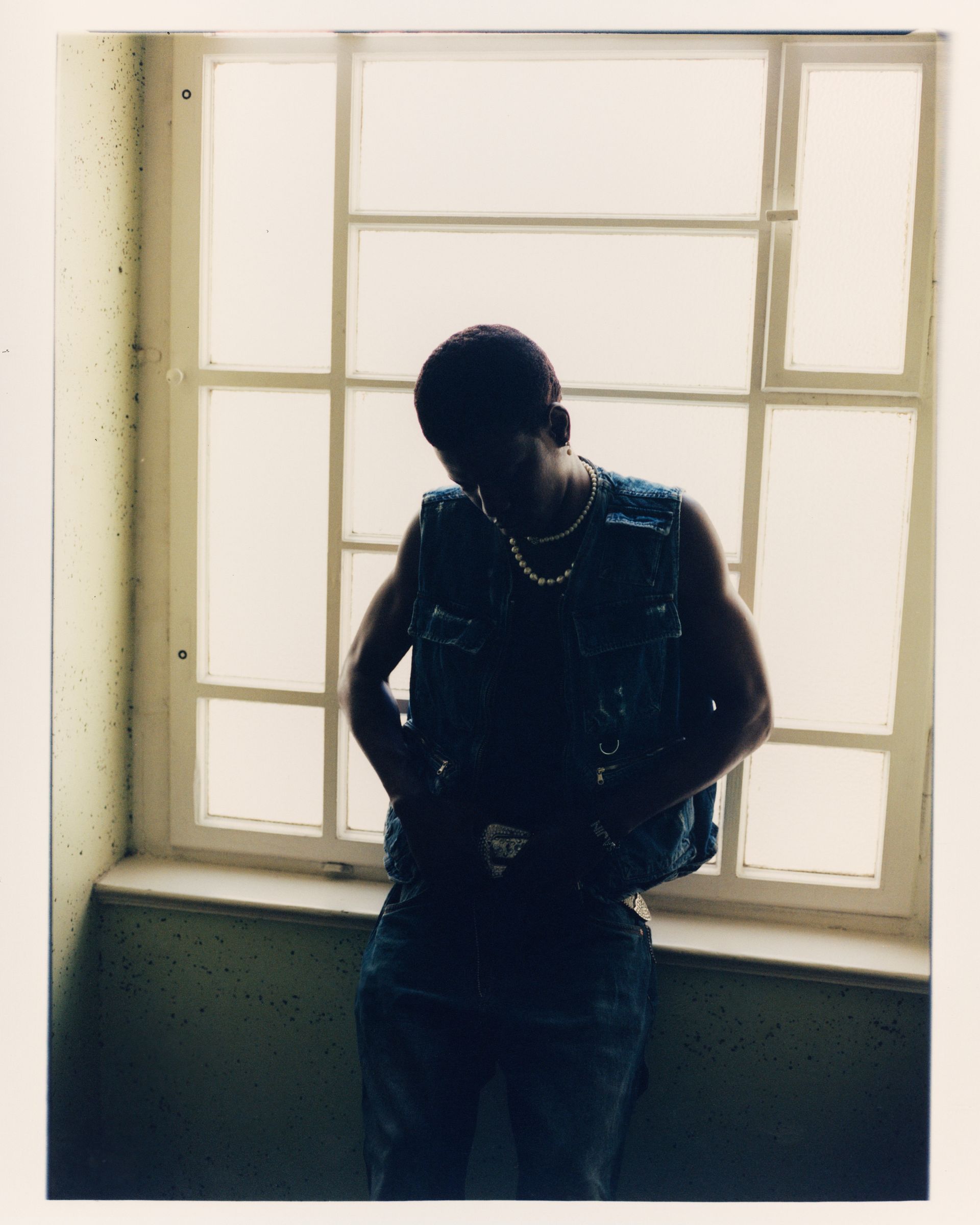 Ein Mann in Jeansweste und Jeans steht an einem Fenster und zeichnet sich als Silhouette gegen das Licht ab.