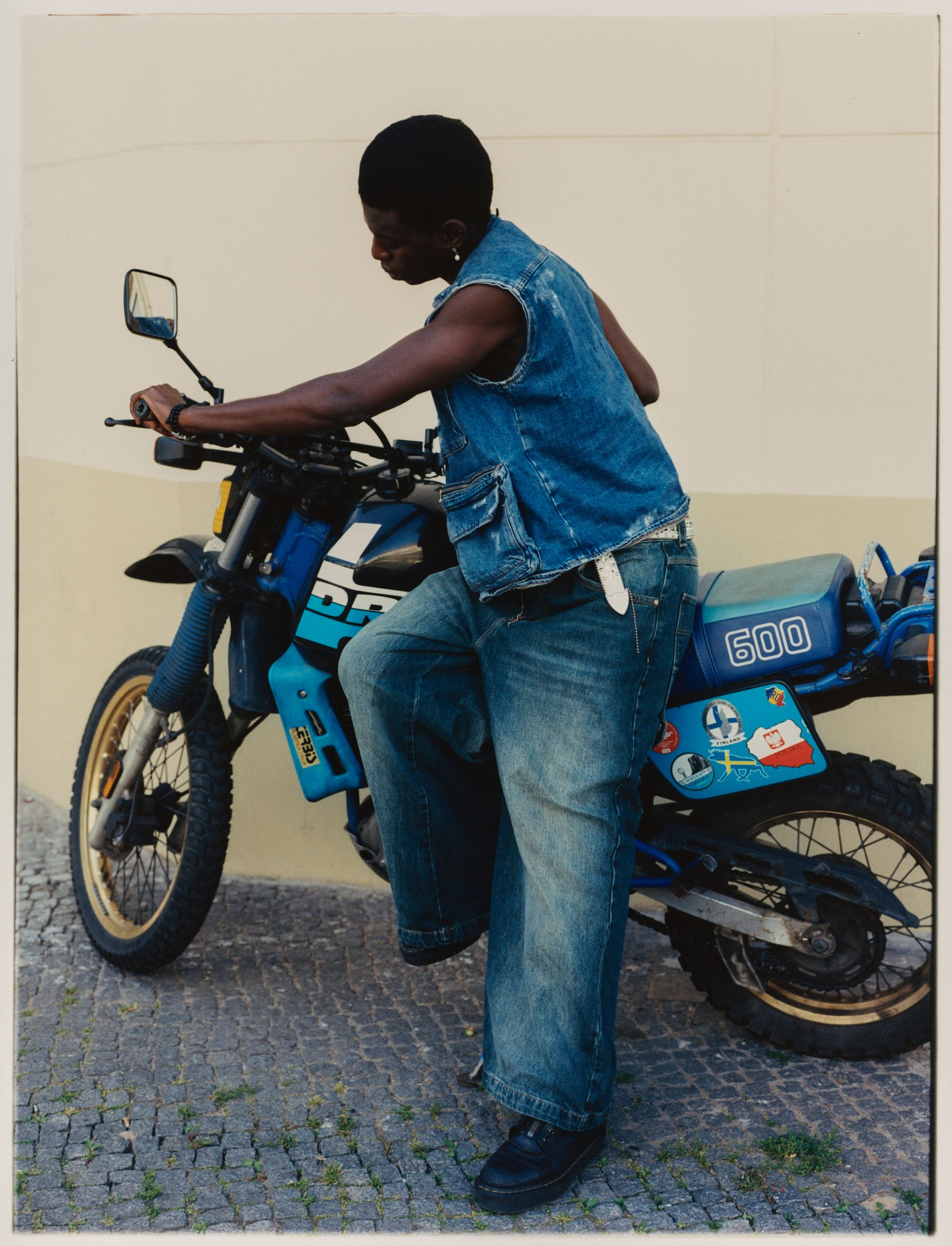 Person im Jeans-Outfit steht neben einem blauen Motorrad.