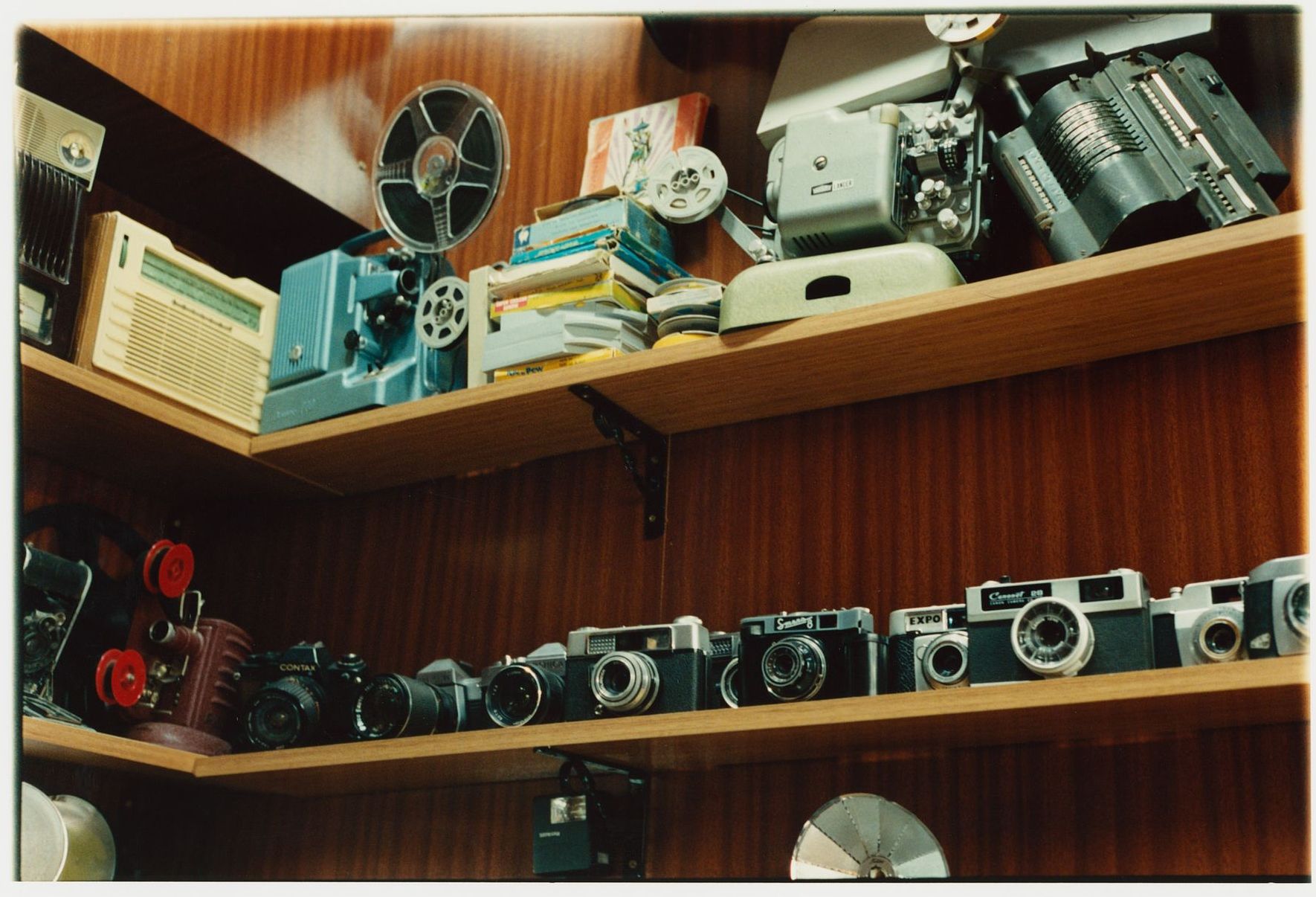 Auf Regalen mit Holzvertäfelung im Hintergrund sind Vintage-Kameras und Filmprojektoren ausgestellt.