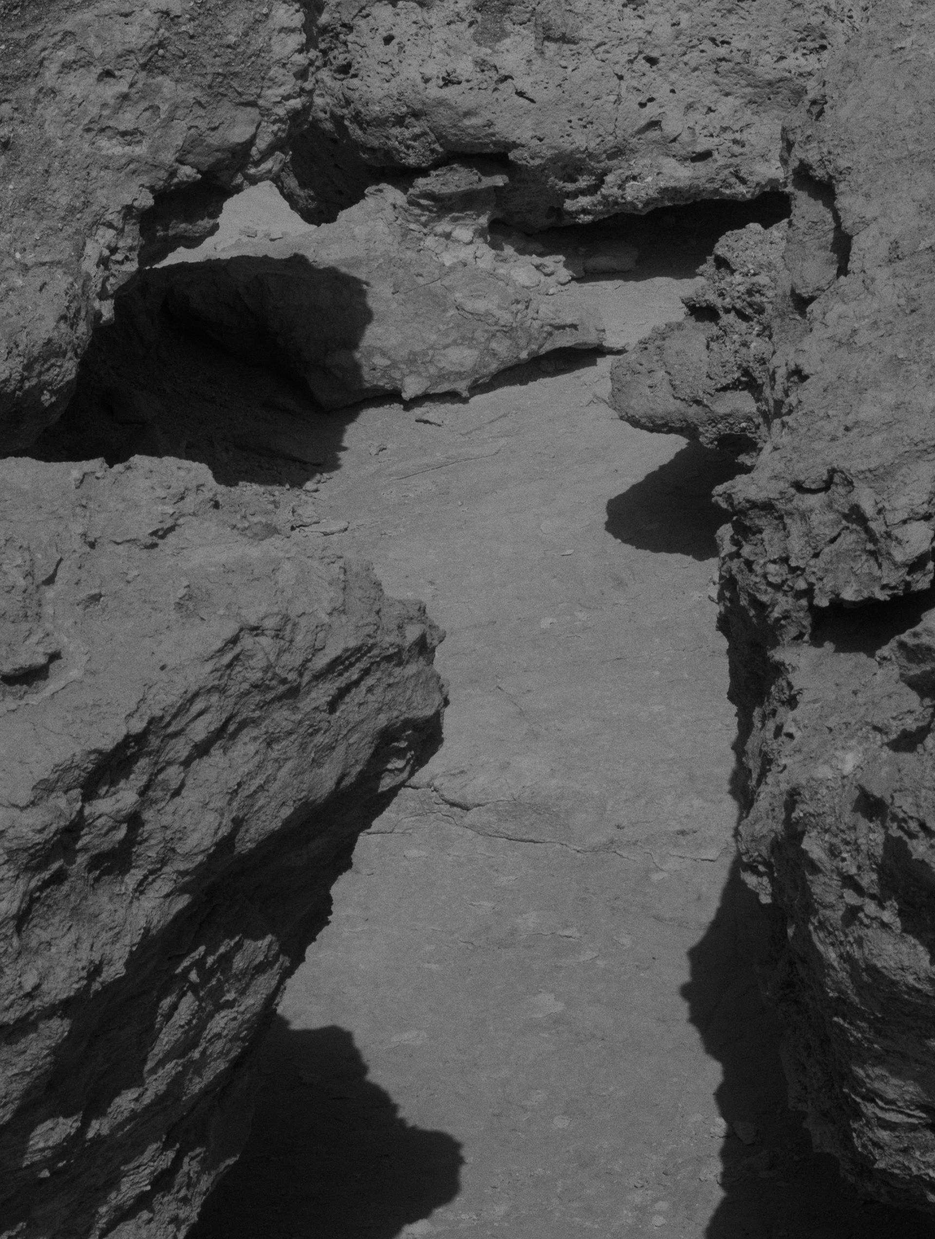 Felsiges Gelände mit einem schmalen, sandigen Pfad zwischen Felsformationen. Schwarz und Weiß.