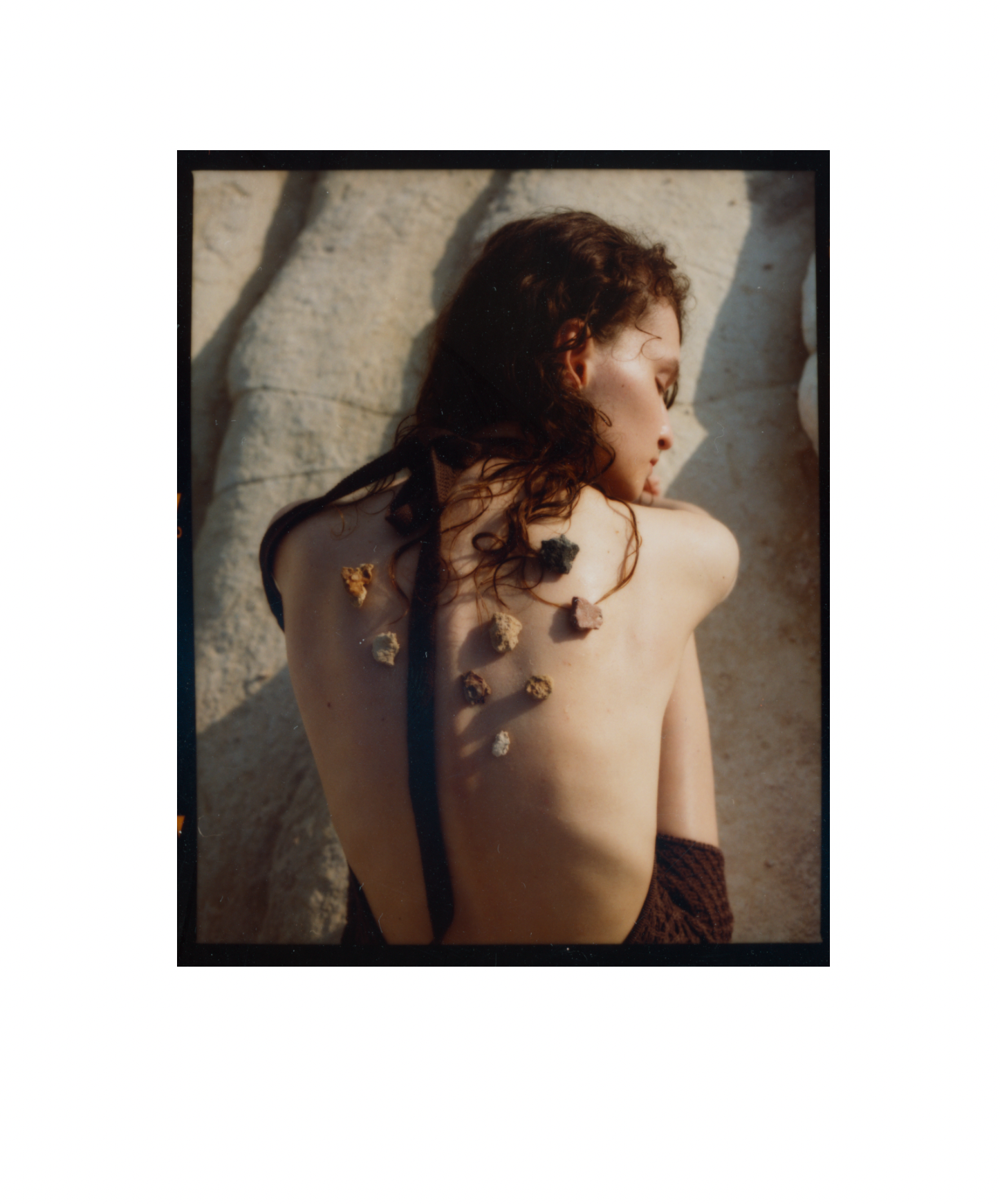 Frau mit Schmuck auf dem Rücken, sonnenbeschienen vor einem Felsen.