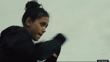 Junge Person in schwarzem Kapuzenpullover, mit erhobenen Fäusten, übt Boxen im Freien.