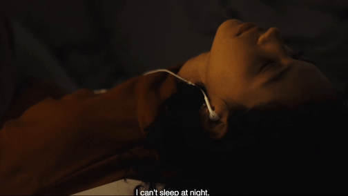 Frau liegt mit geschlossenen Augen und Ohrstöpseln in einem schwach beleuchteten Raum im Bett. 