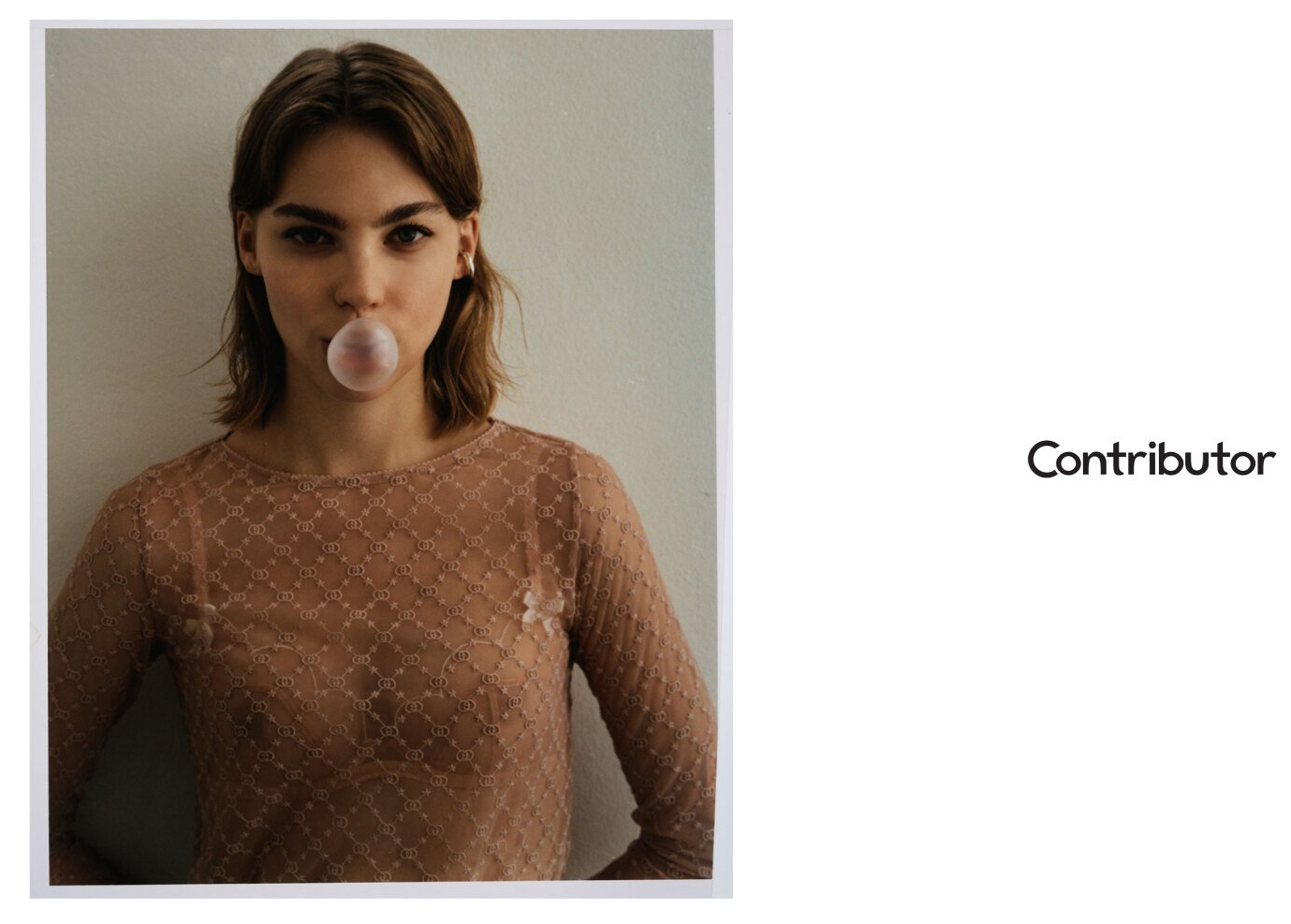 Frau, die Seifenblasen macht, ein durchsichtiges braunes Oberteil trägt und vor einer schlichten Wand steht.