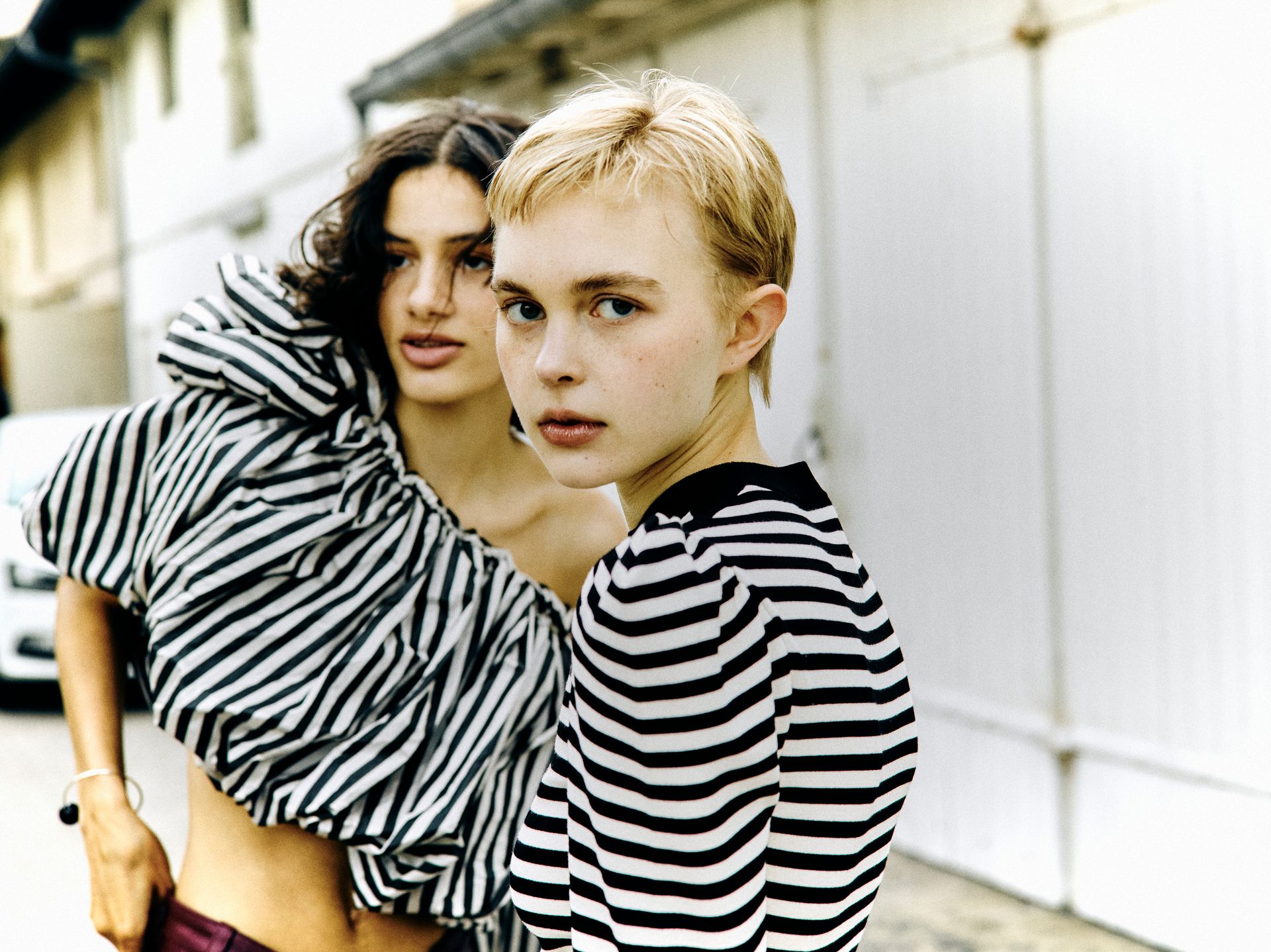 Zwei junge Menschen in gestreiften Oberteilen posieren im Freien. Einer mit kurzen blonden Haaren blickt in die Kamera.