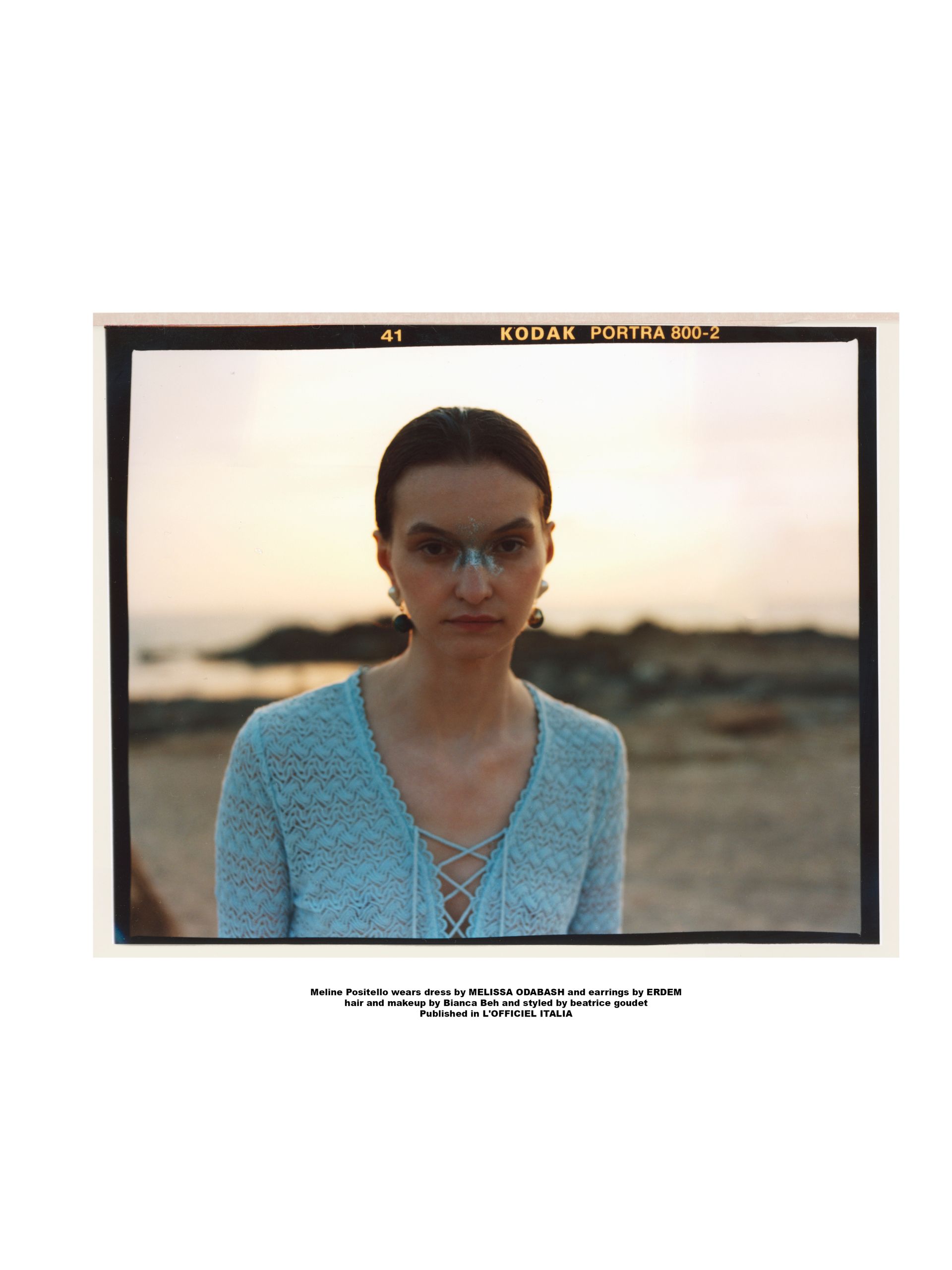 Frau in einem hellblauen Spitzentop, Strandhintergrund. Sie trägt eine Brille und Ohrringe, Sonnenuntergang.