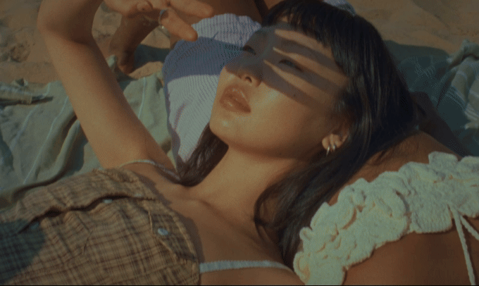 Frau sonnt sich am Strand und beschattet ihre Augen mit der Hand. Sanfte Beleuchtung, warme Töne.