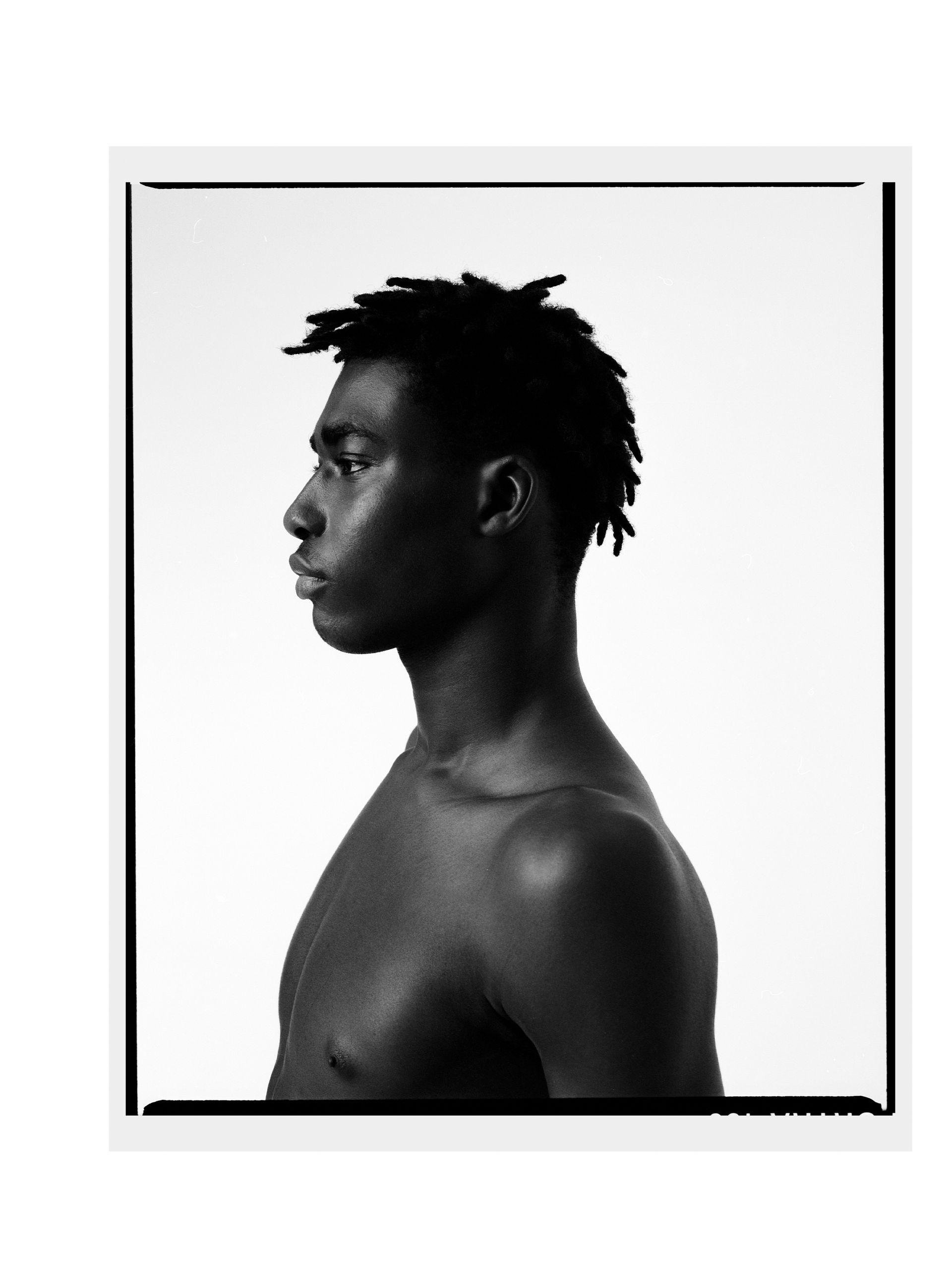 Schwarz-Weiß-Porträt eines oberkörperfreien schwarzen Mannes im Profil, der nach links blickt.