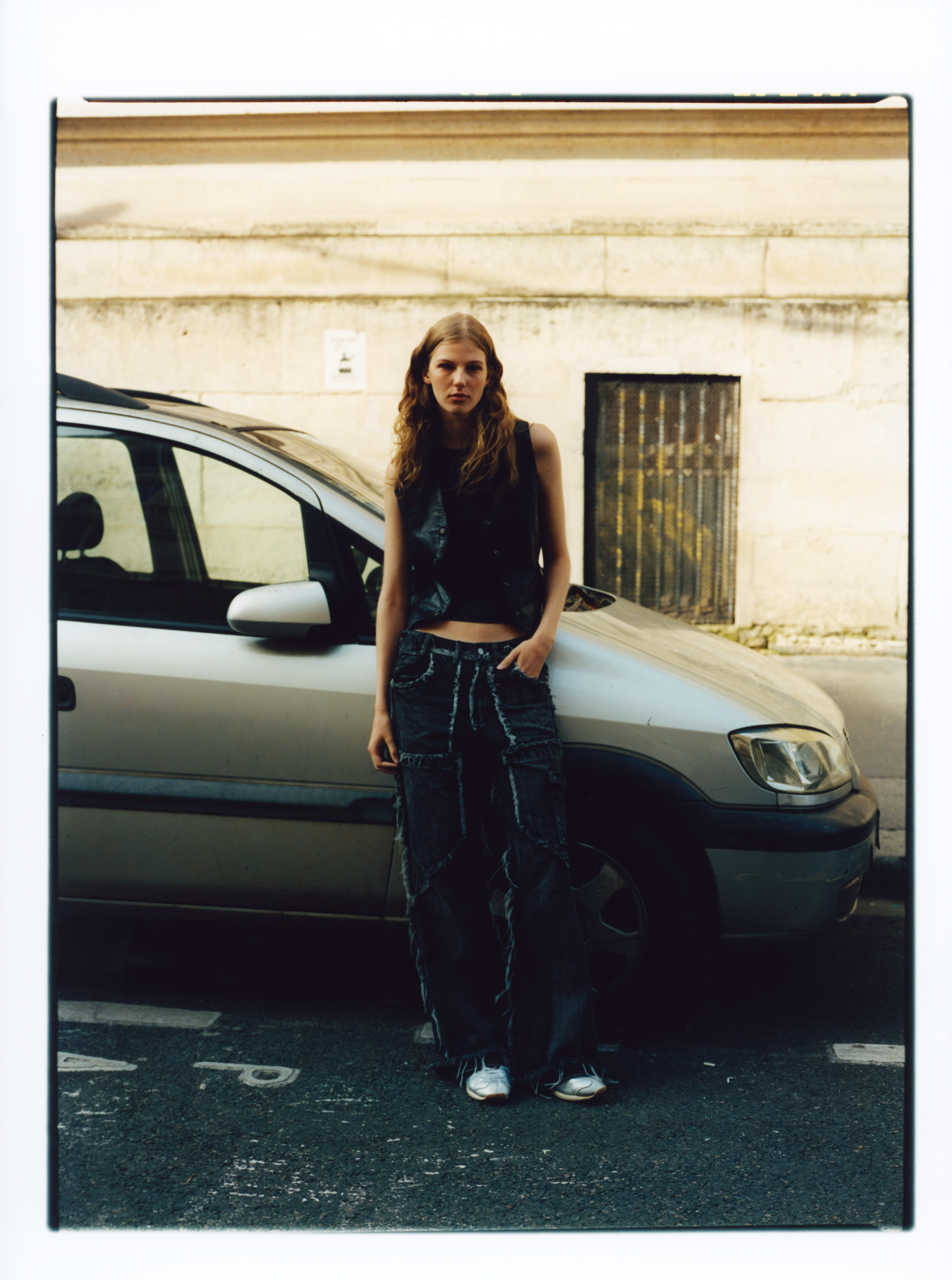 Frau in dunklem Outfit lehnt auf einer Stadtstraße an einem silbernen Auto.